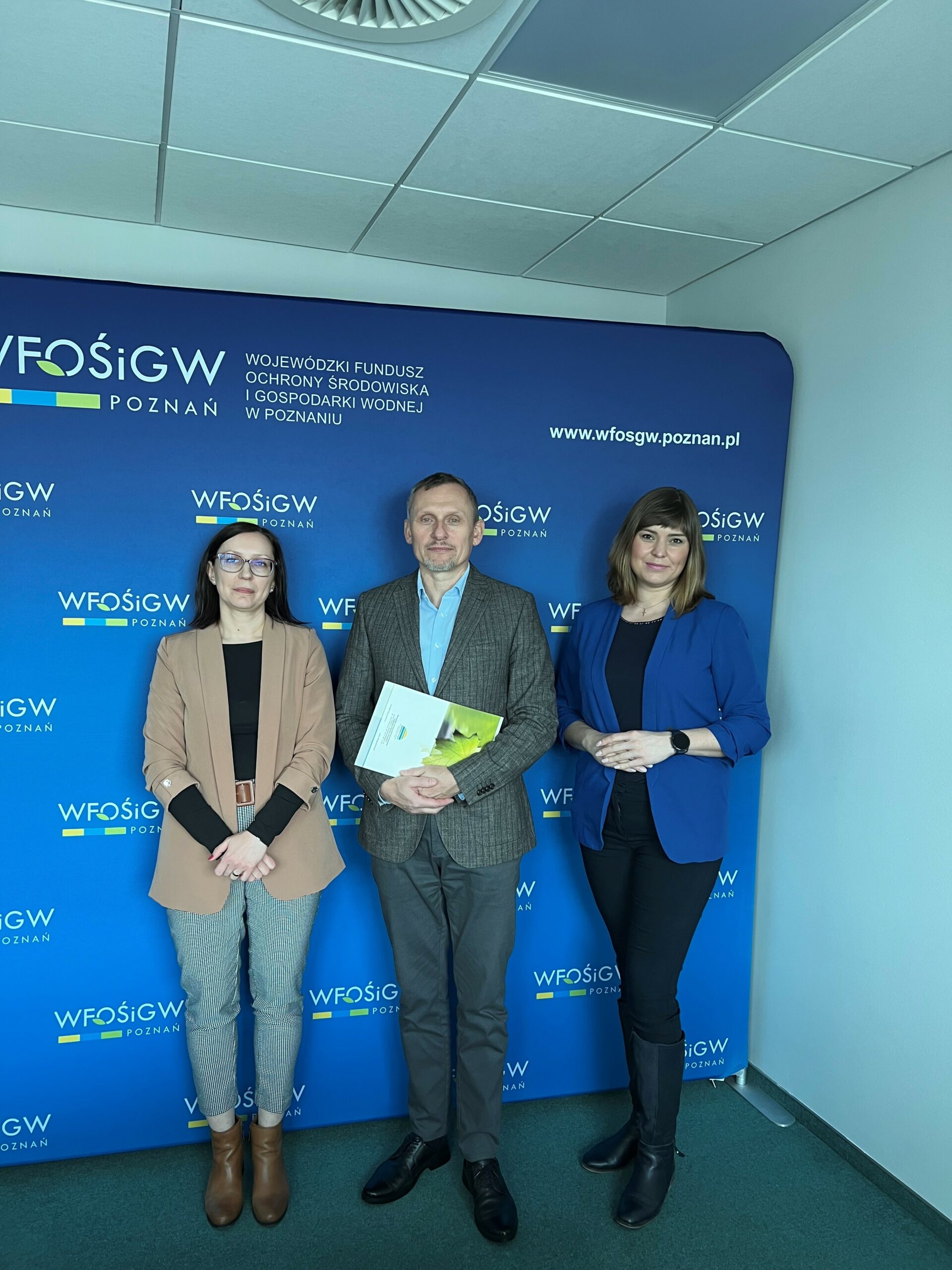 3 osoby stoją na tle ściany.