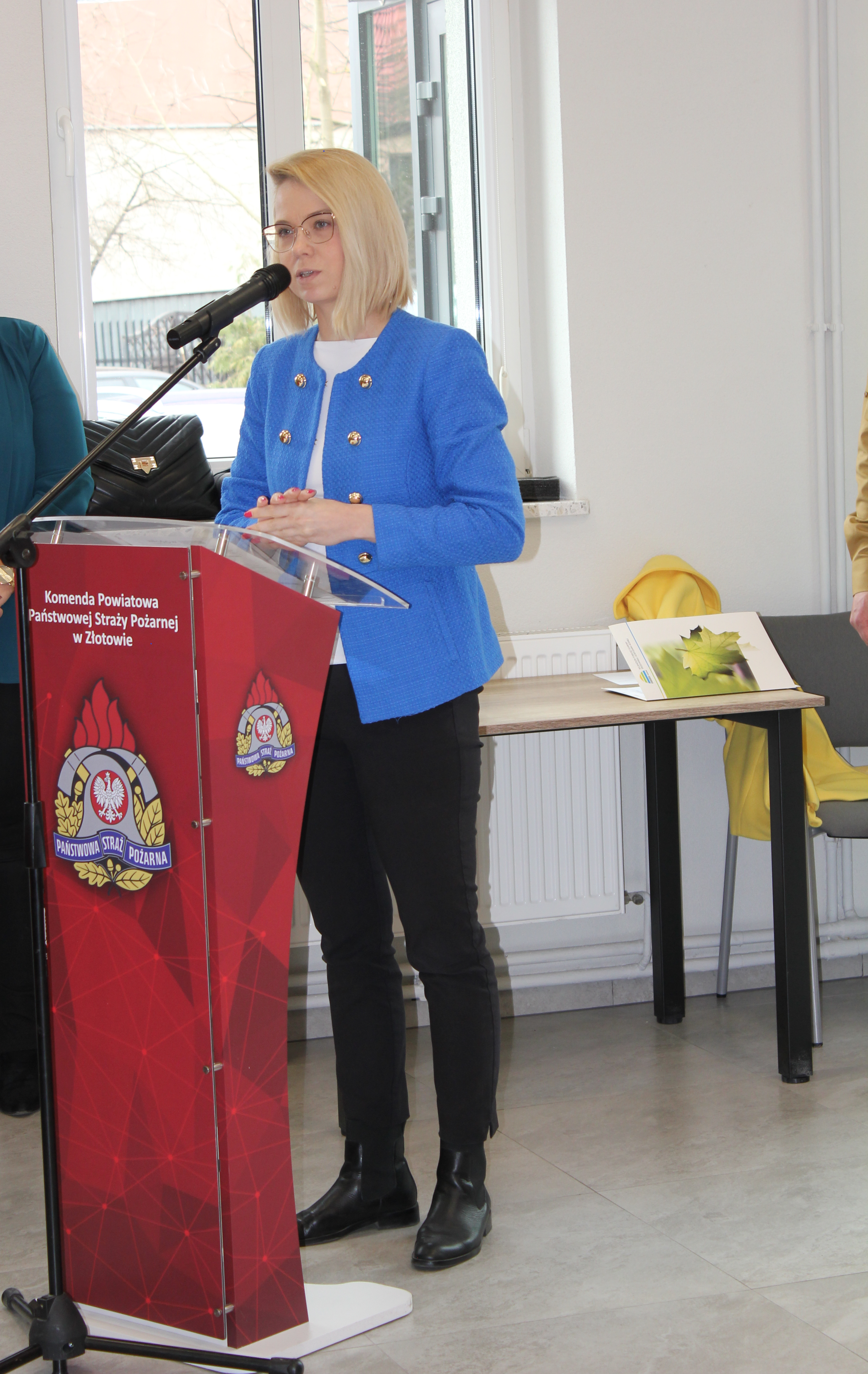 1 osoba stoi przy mównicy i przemawia.