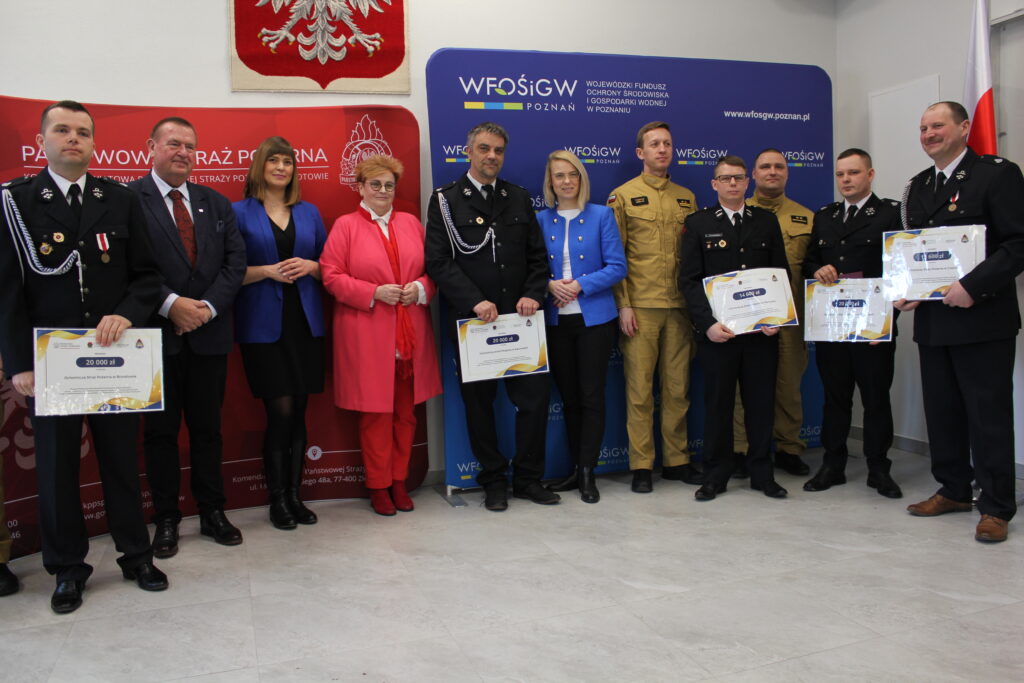 Grupa osób stoi na sali na tle ściany i bannerów reklamowych.