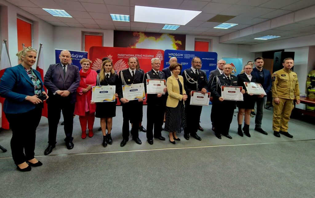 Grupa osób stoi na tle ściany i bannerów reklamowych.