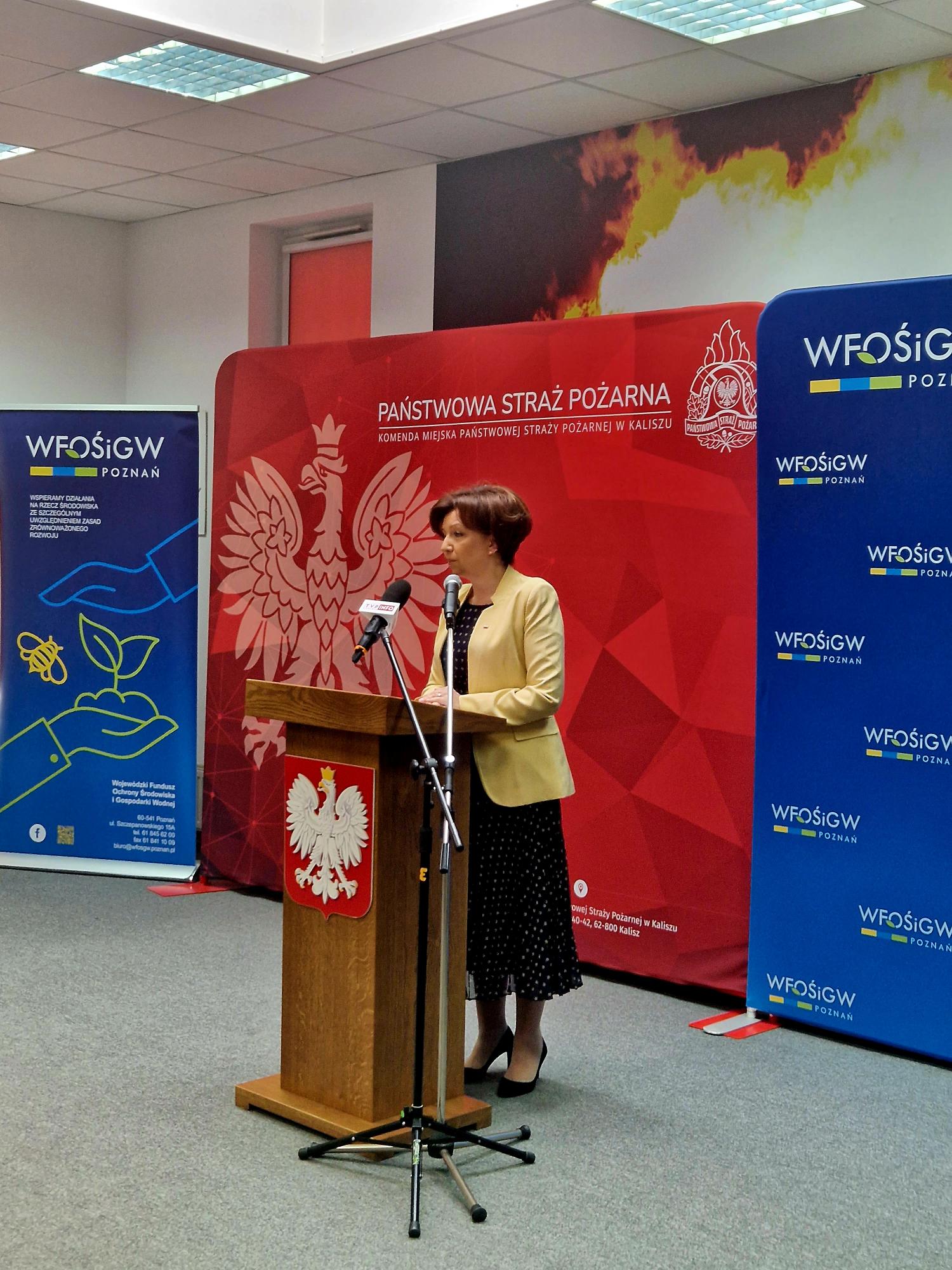 1 osoba stoi przy mównicy i przemawia.