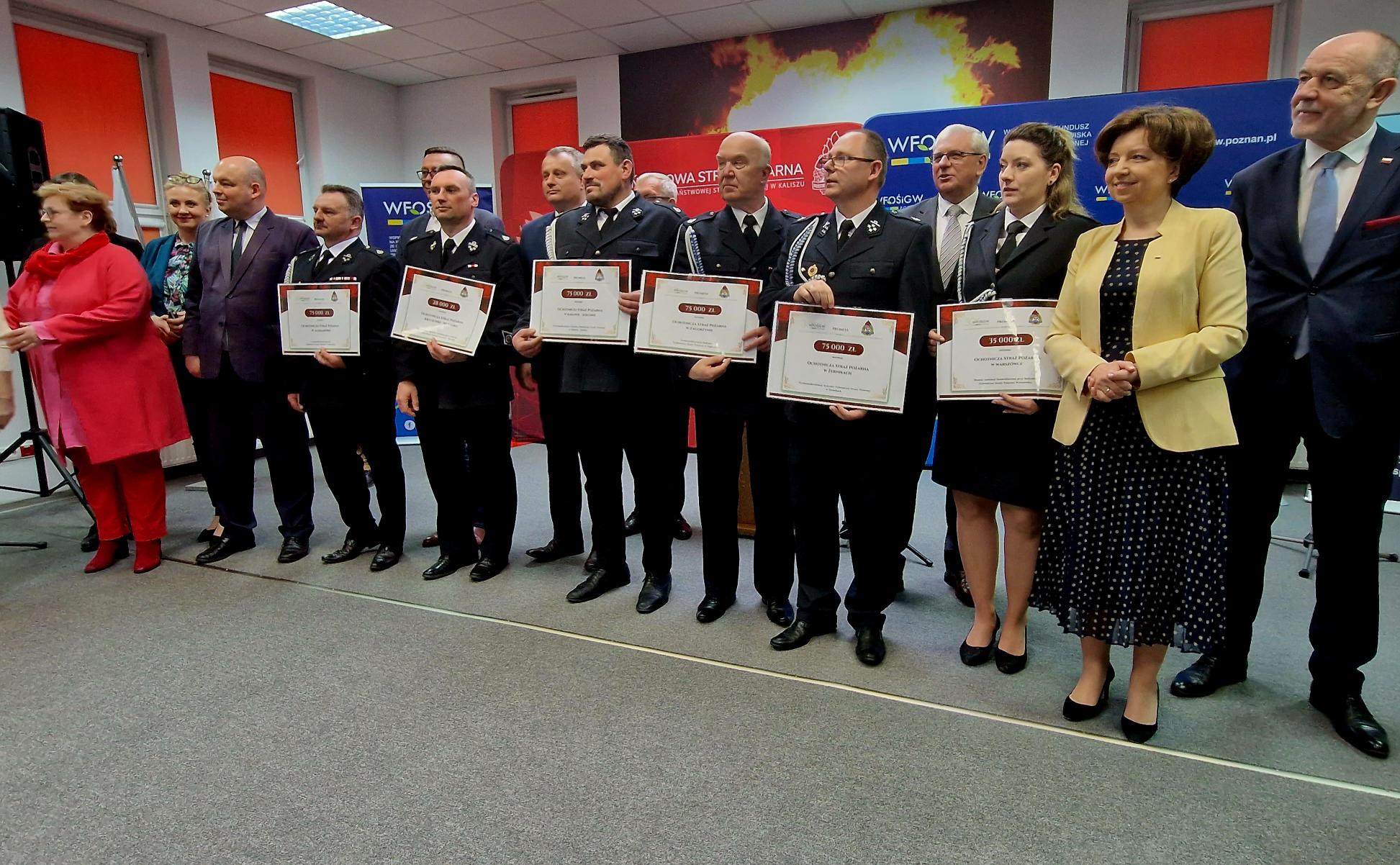 Grupa osób stoi na tle bannerów reklamowych.