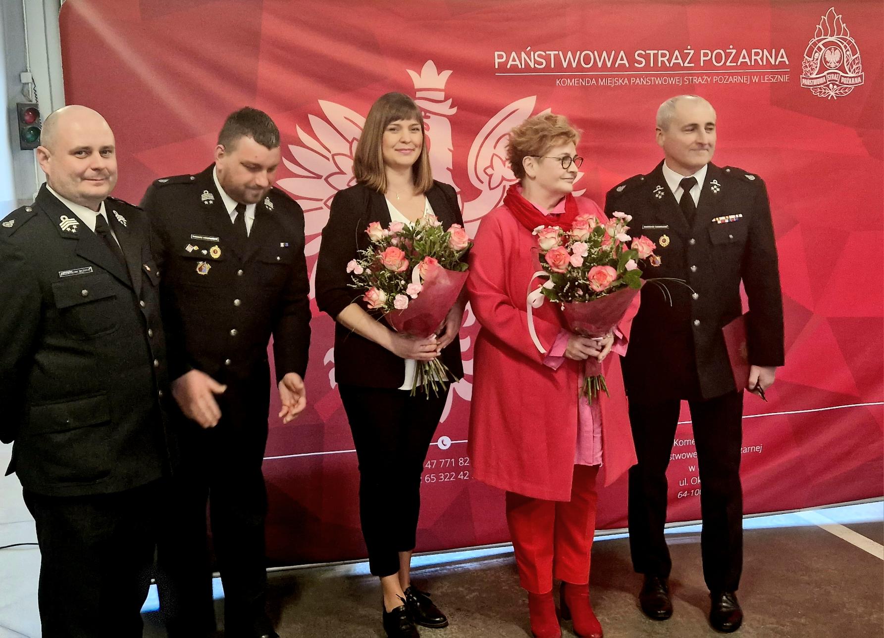 5 osób stoi na tle bannerów reklamowych.