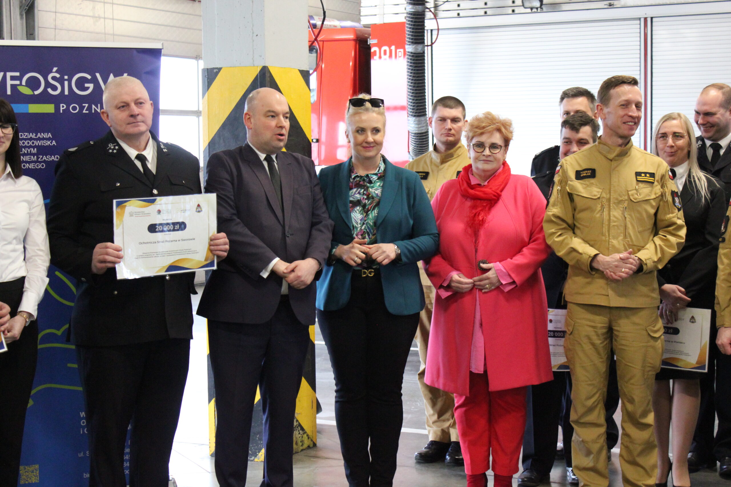 Grupa osób stoi na tle ścianek reklamowych.