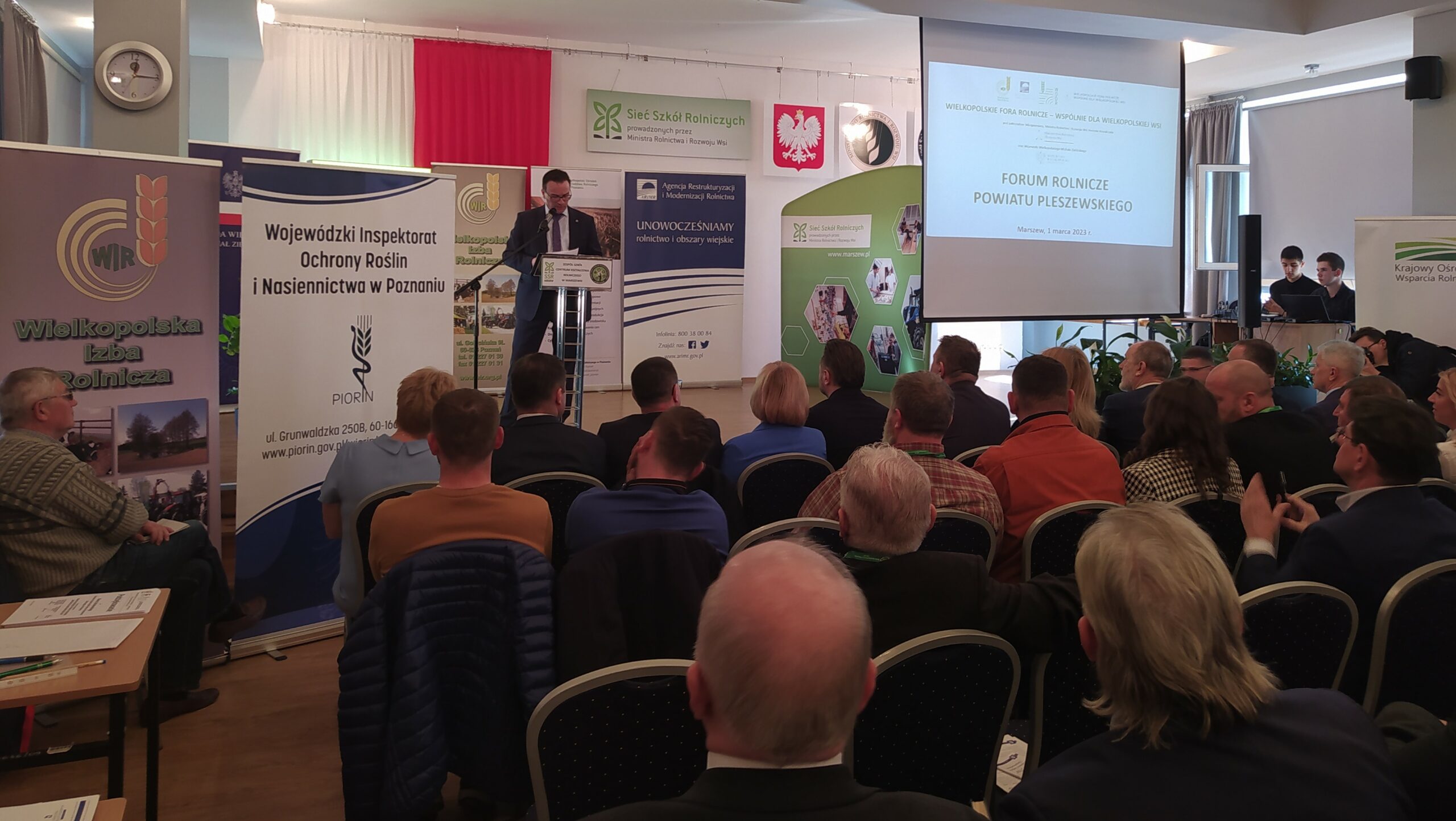 Sala pena ludzi, a jedna osoba przemawia.