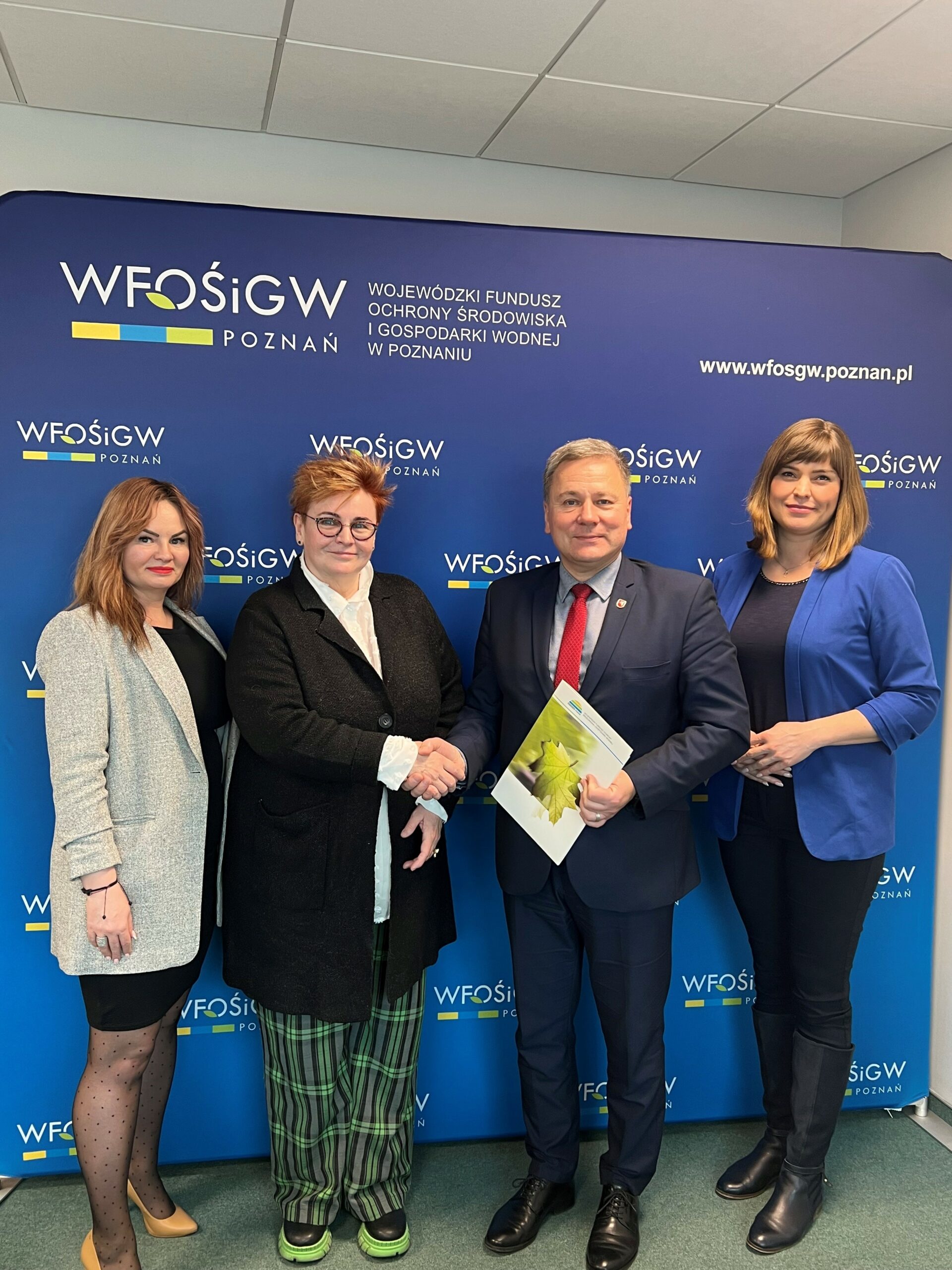 4 osoby stoją na tle ściany.