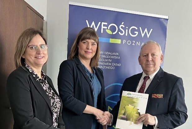 3 osoby stoją na tlę ściany i bannera reklamowego.