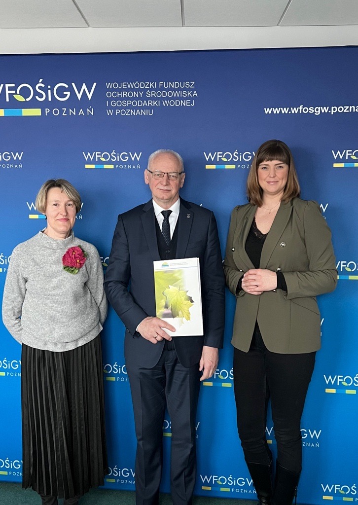 3osoby stoją na tle ściany i bannera reklamowego.