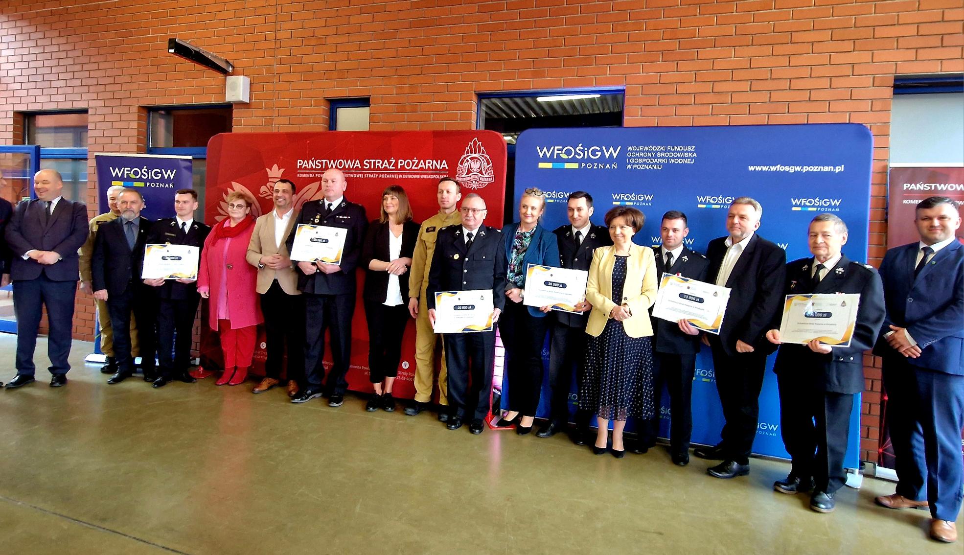 Grupa osób stoi przy ścianie na tle ścianek reklamowych.