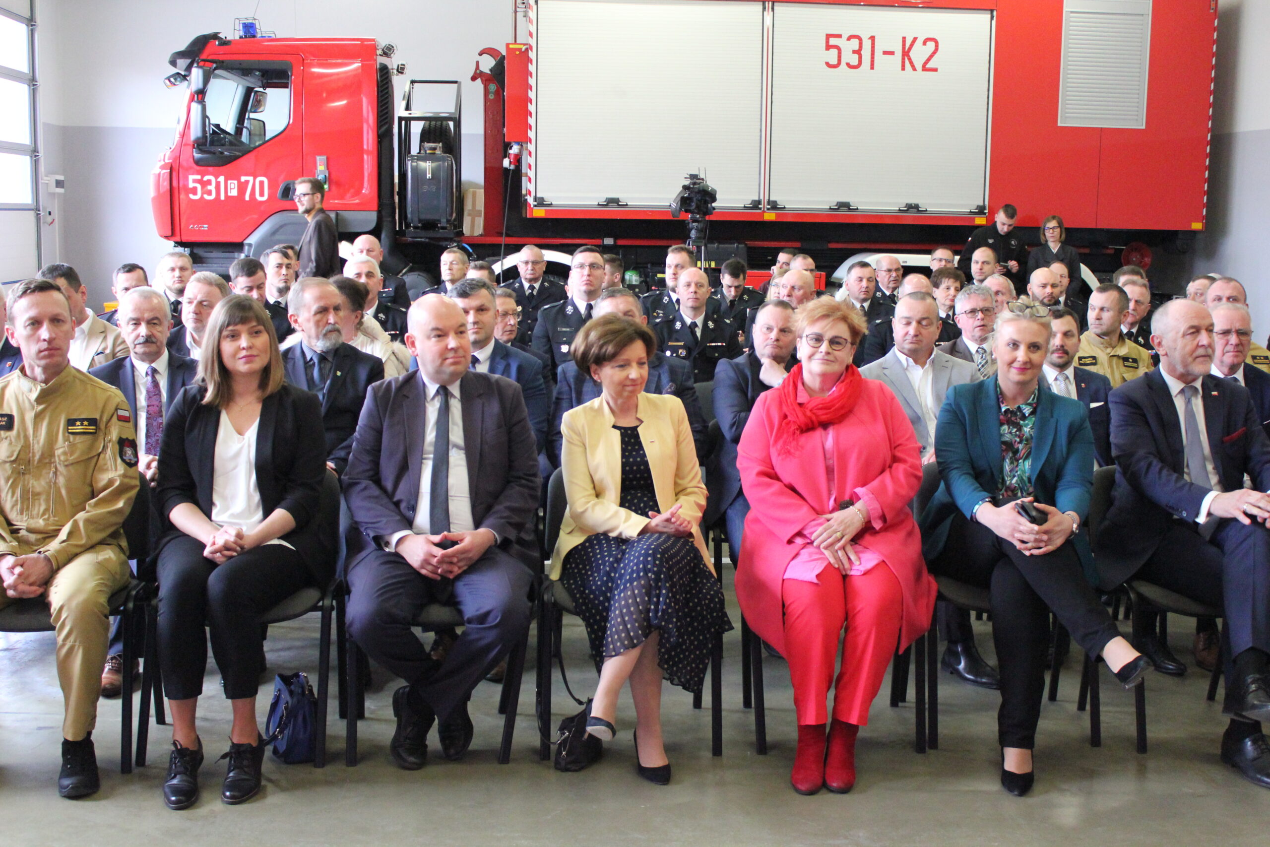 Ludzie siedzący na krzesłach na dużej sali (garaż straży pożarnej.