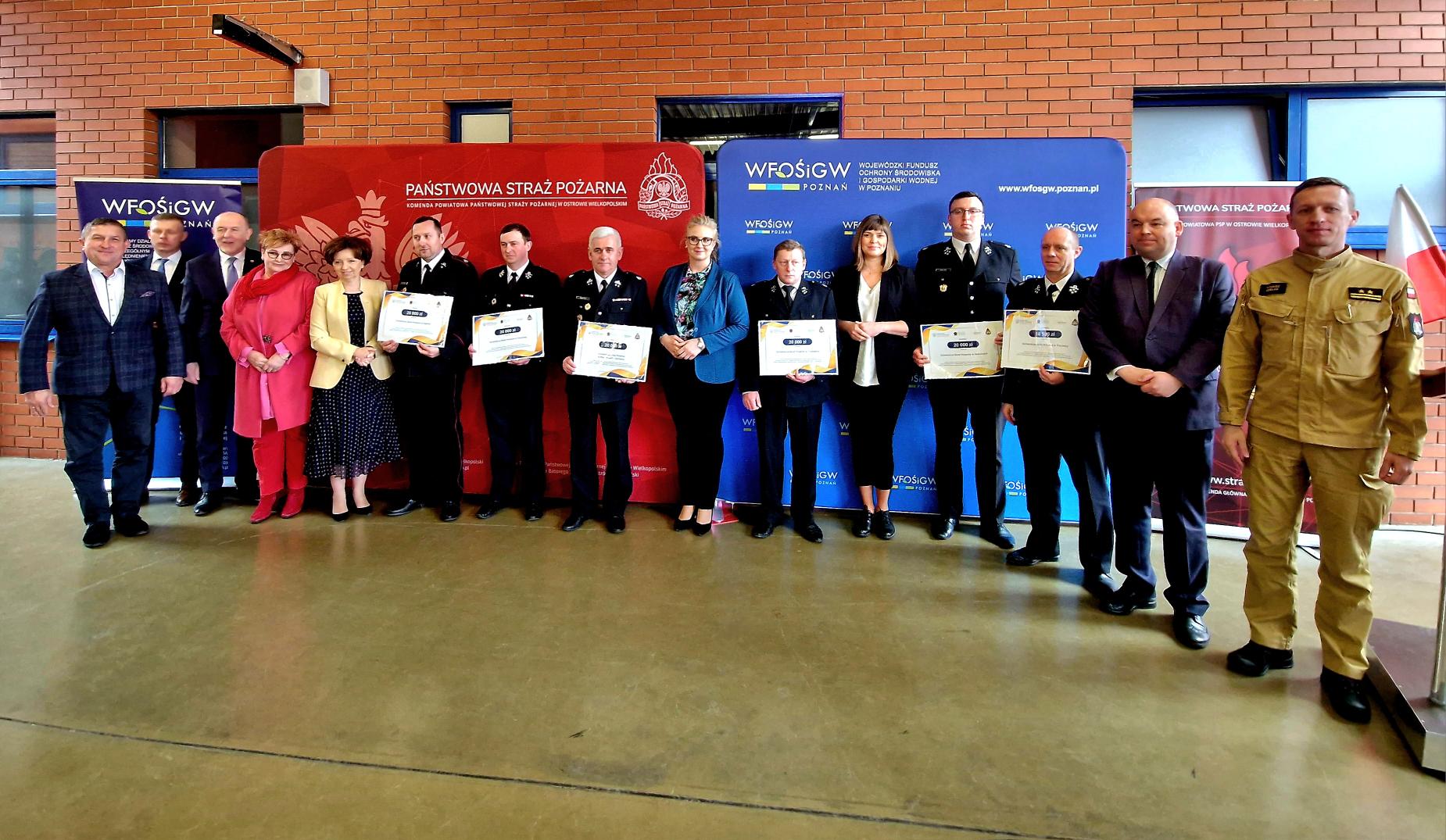 Grupa osób stoi na tle ścianek reklamowych.