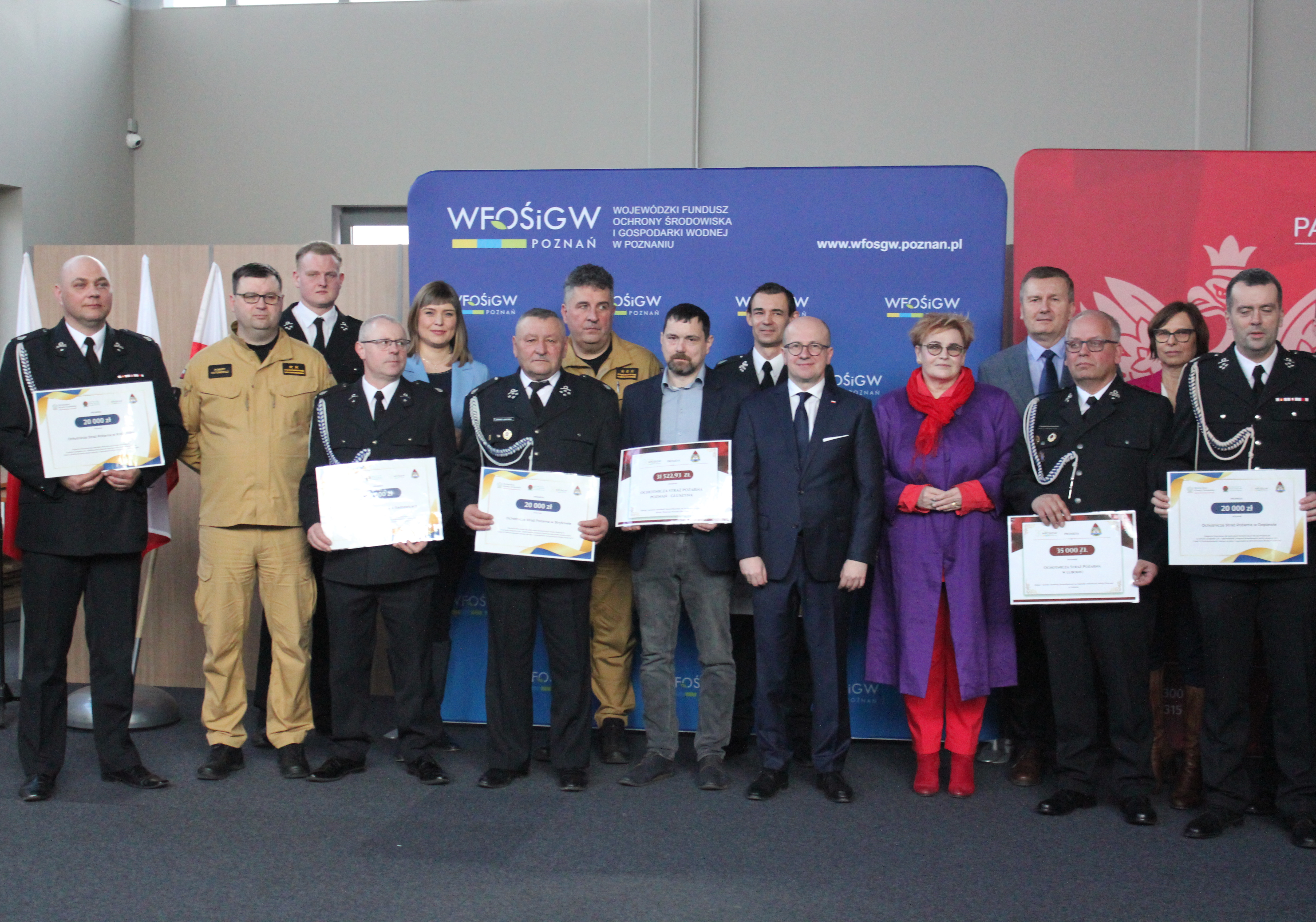 Grupa osób stoi na tle ścianek reklamowych.