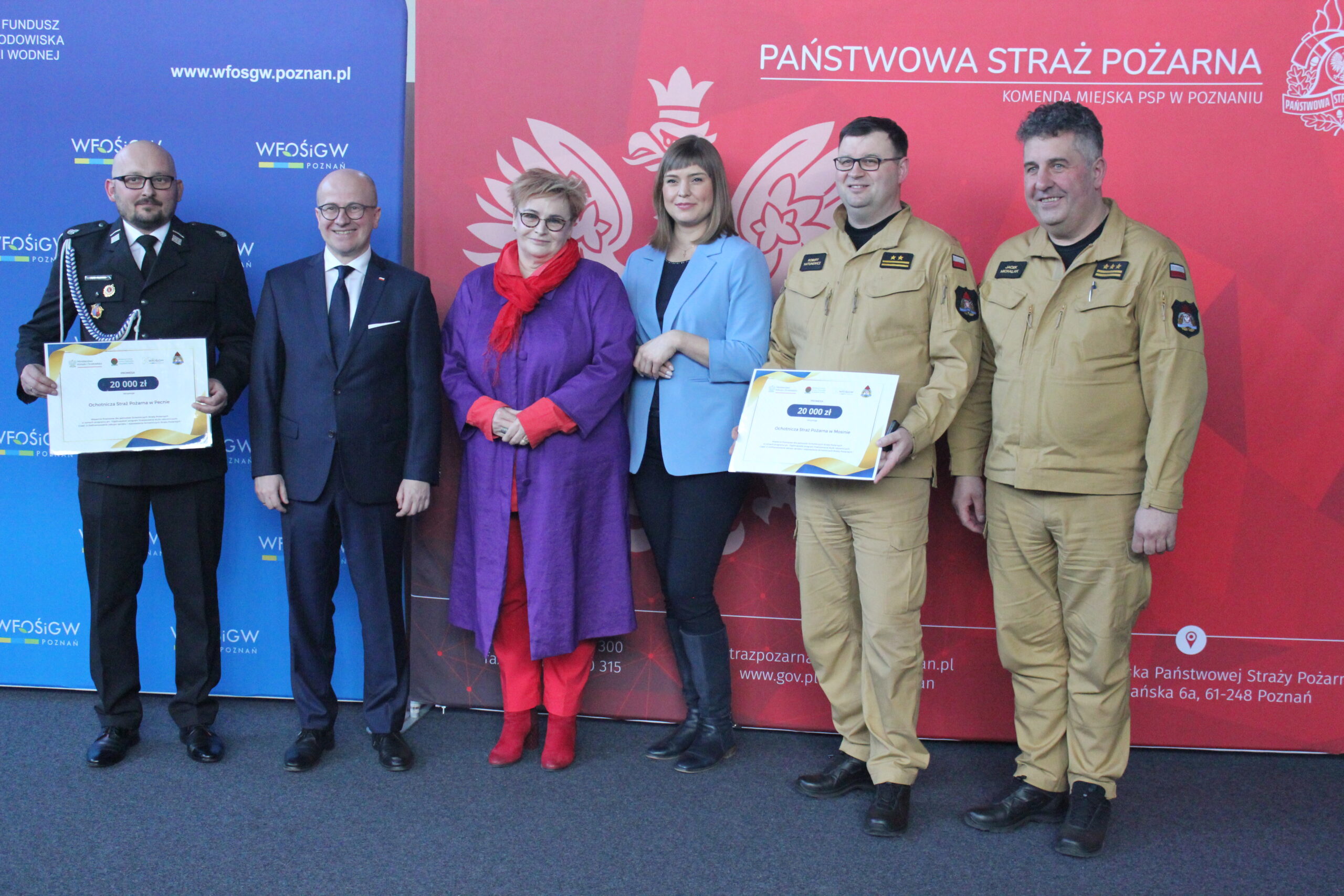 Grupa osób stoi na tle ścianek reklamowych i pozuje do zdjęcia.