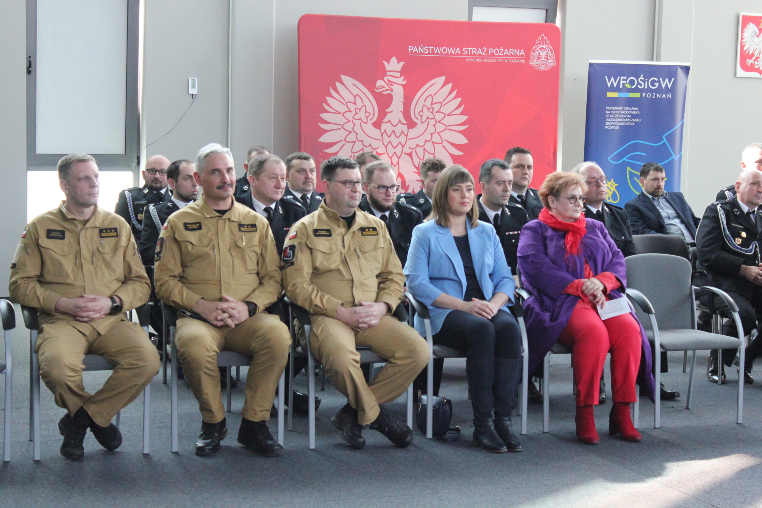 Grupa osób siedzi na sali na krzesłach.