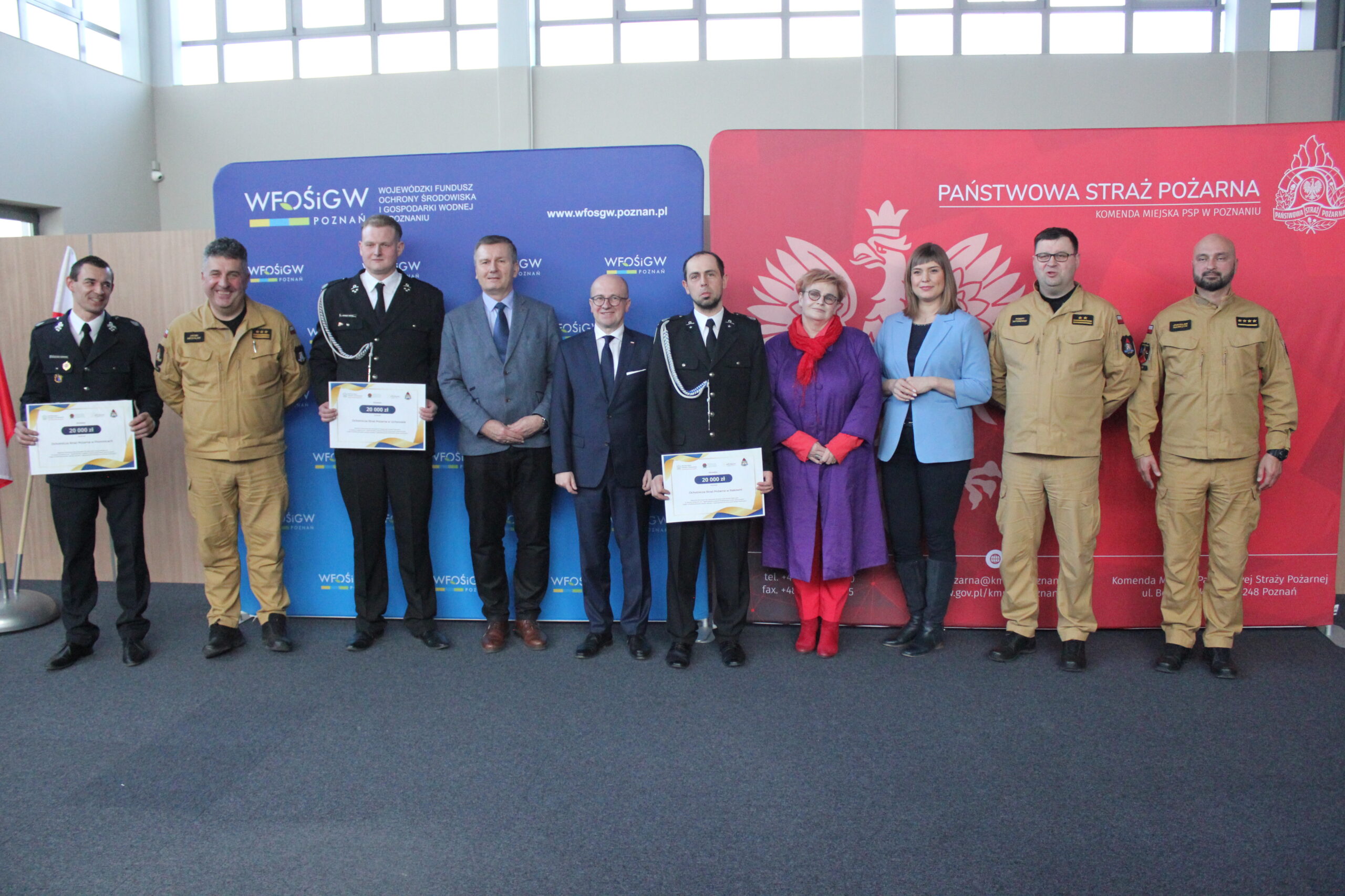 Grupa osób stoi na tle ścianek reklamowych i pozuje do zdjęcia.