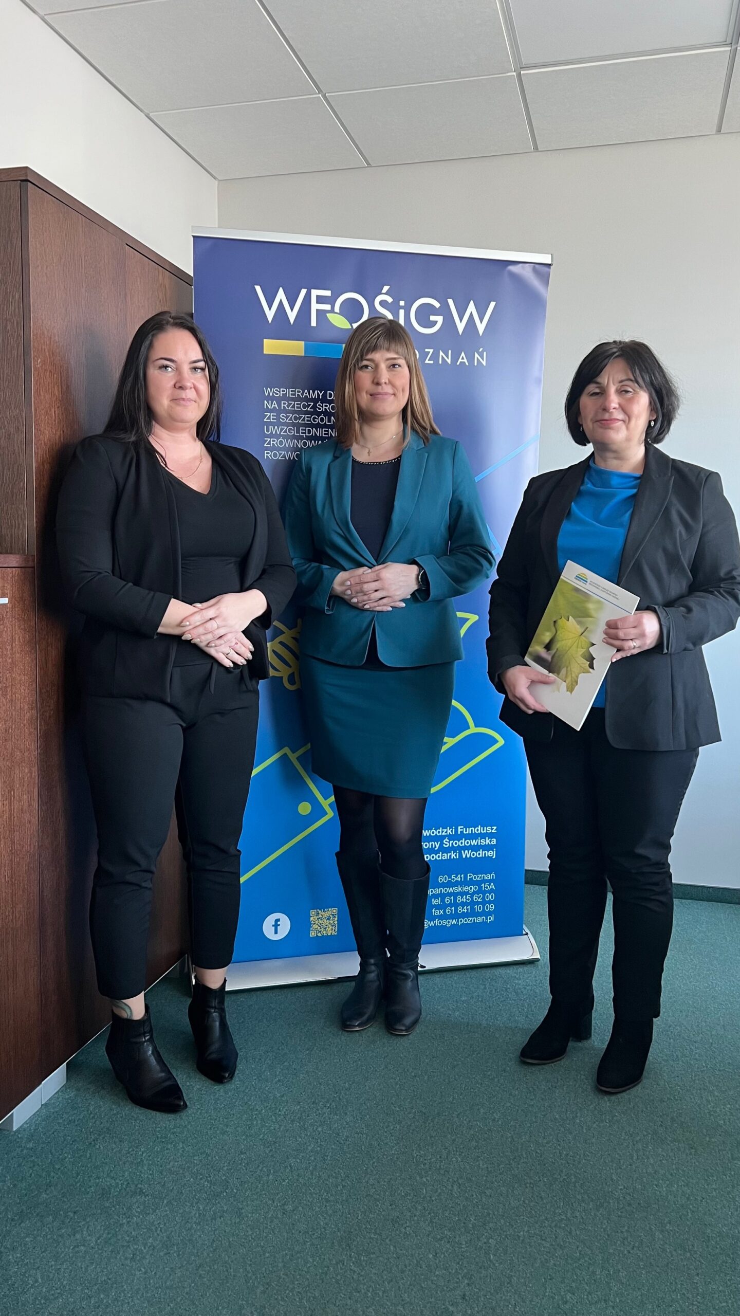 3 osoby stoją na tle ściany i bannera reklamowego.