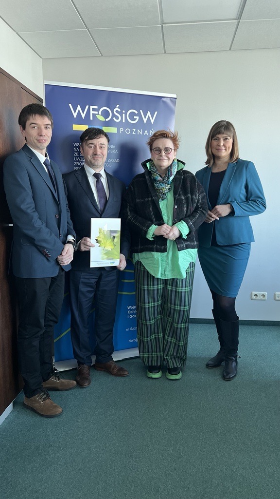 4 osoby stoją na tle ściany i bannera reklamowego.