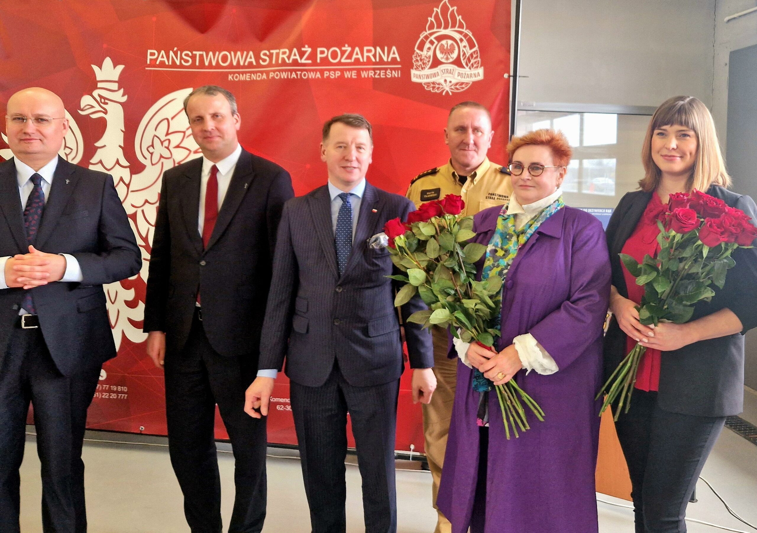 8 osób stoi na tle ściany.