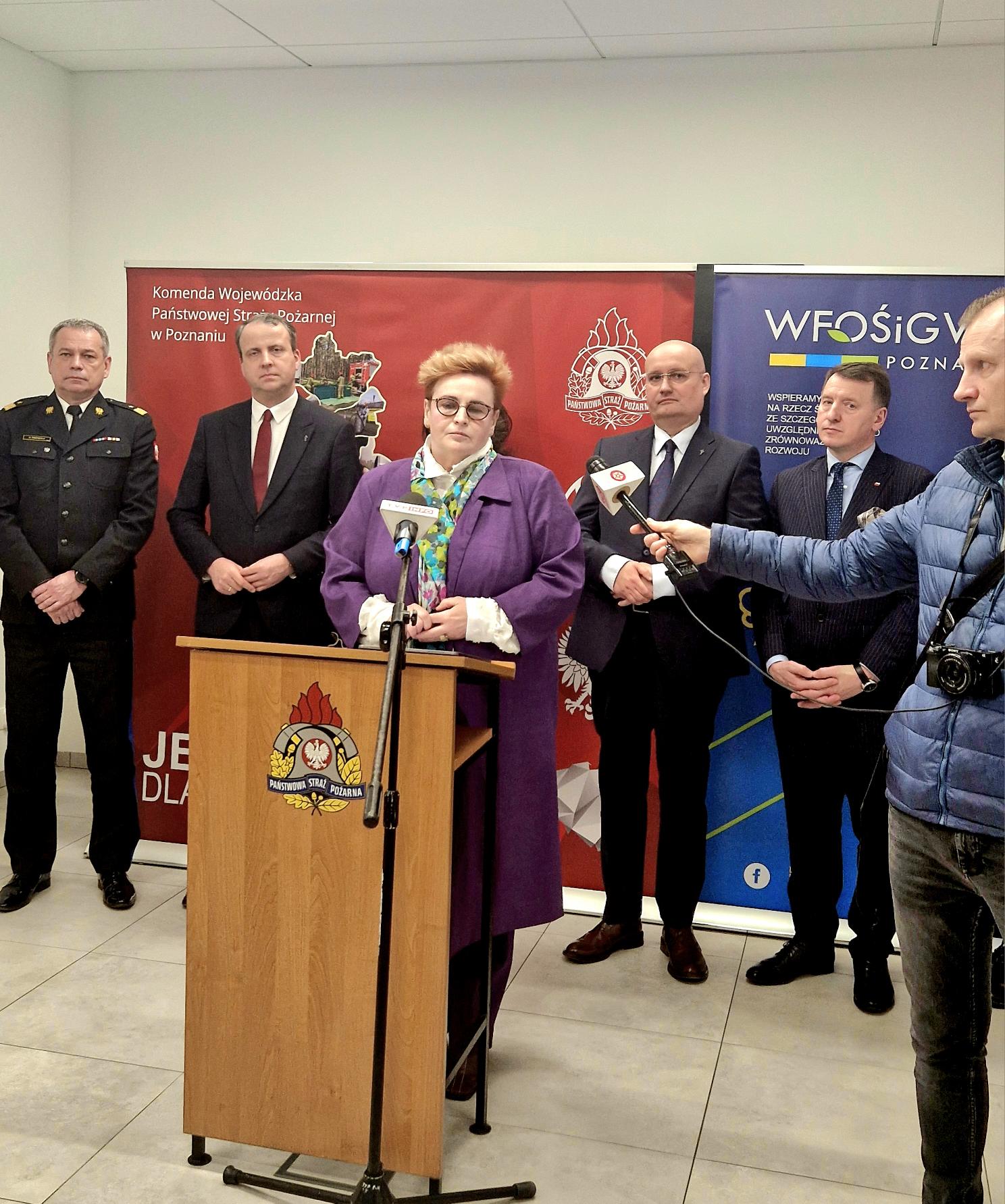 1 osoba stoi przy mównicy i przemawia.