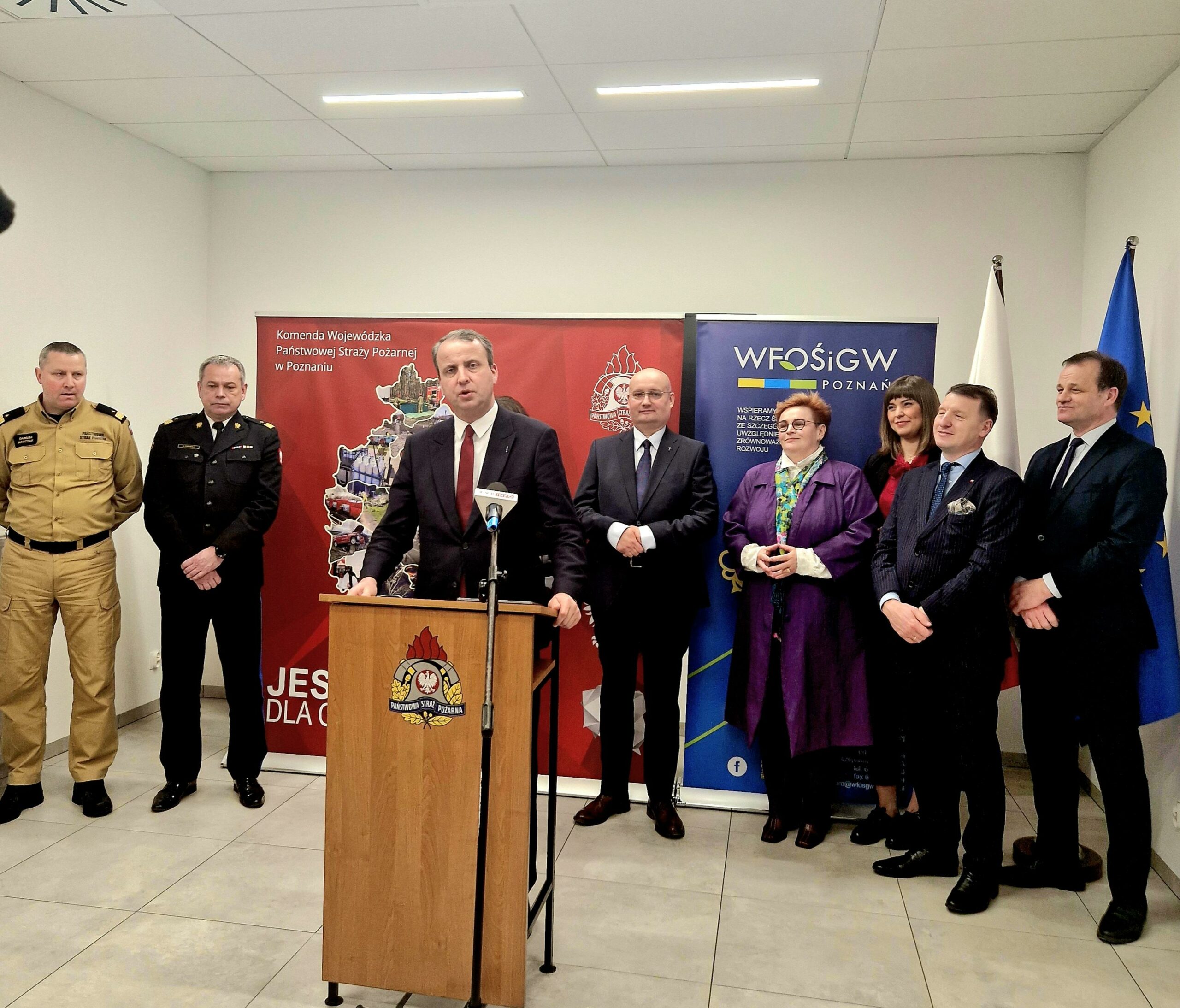 1 osoba stoi przy mównicy i przemawia.