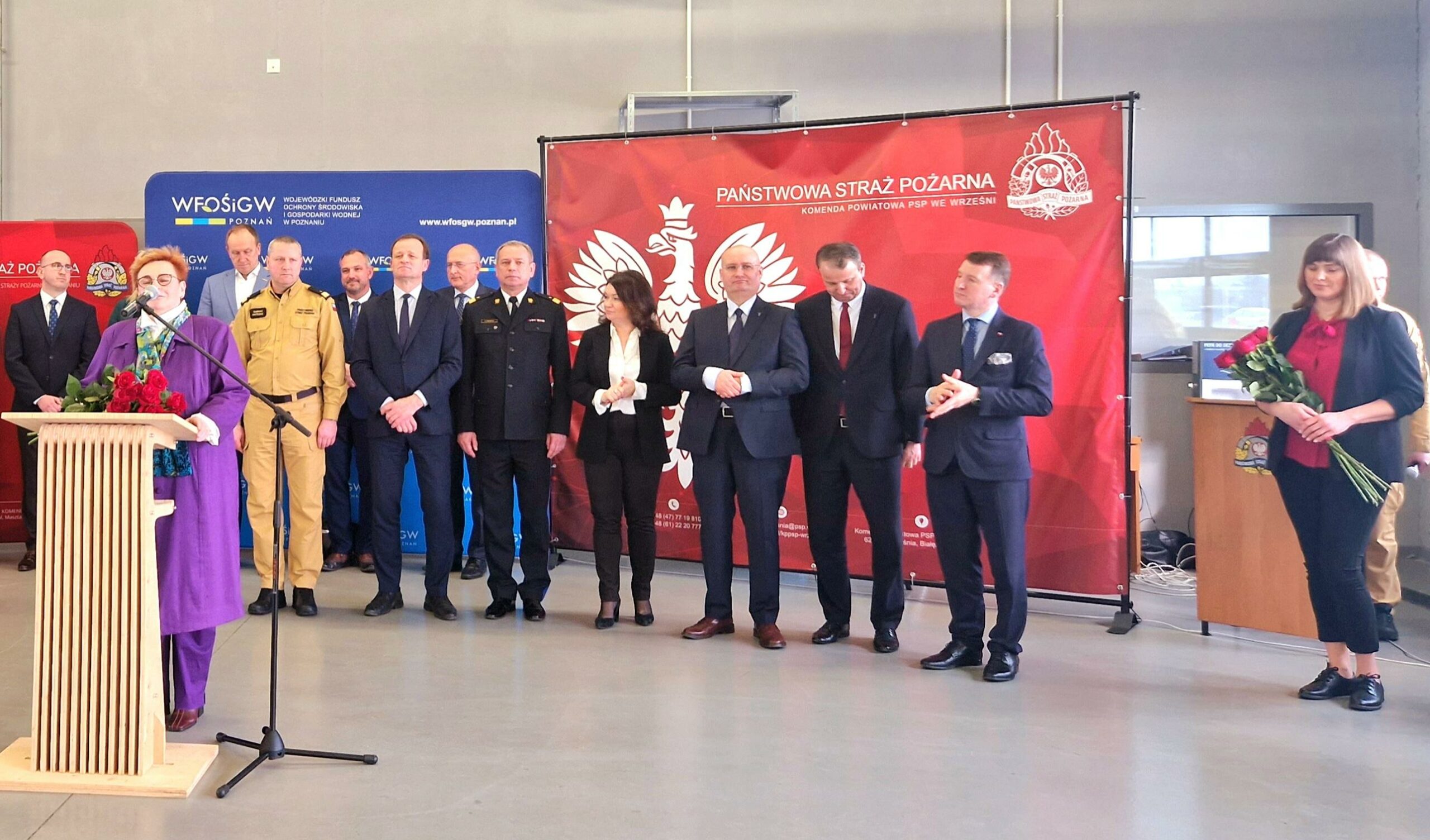 Grupa osób stoi na tle ściany, a jedna osoba stoi przy mównicy.