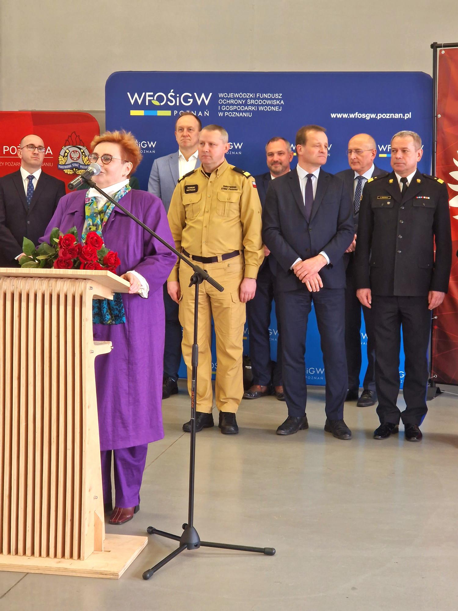 1 osoba stoi przy mównicy i przemawia.