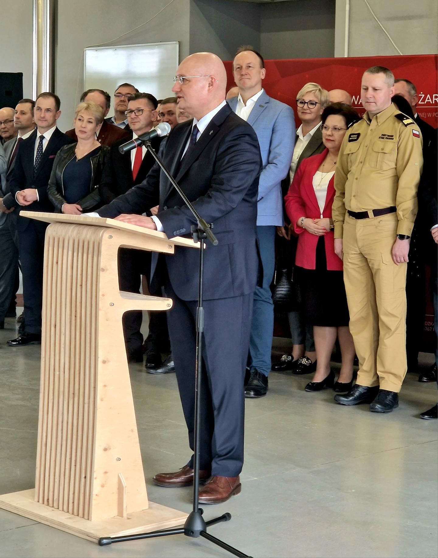 1 osoba stoi przy mównicy i przemawia.