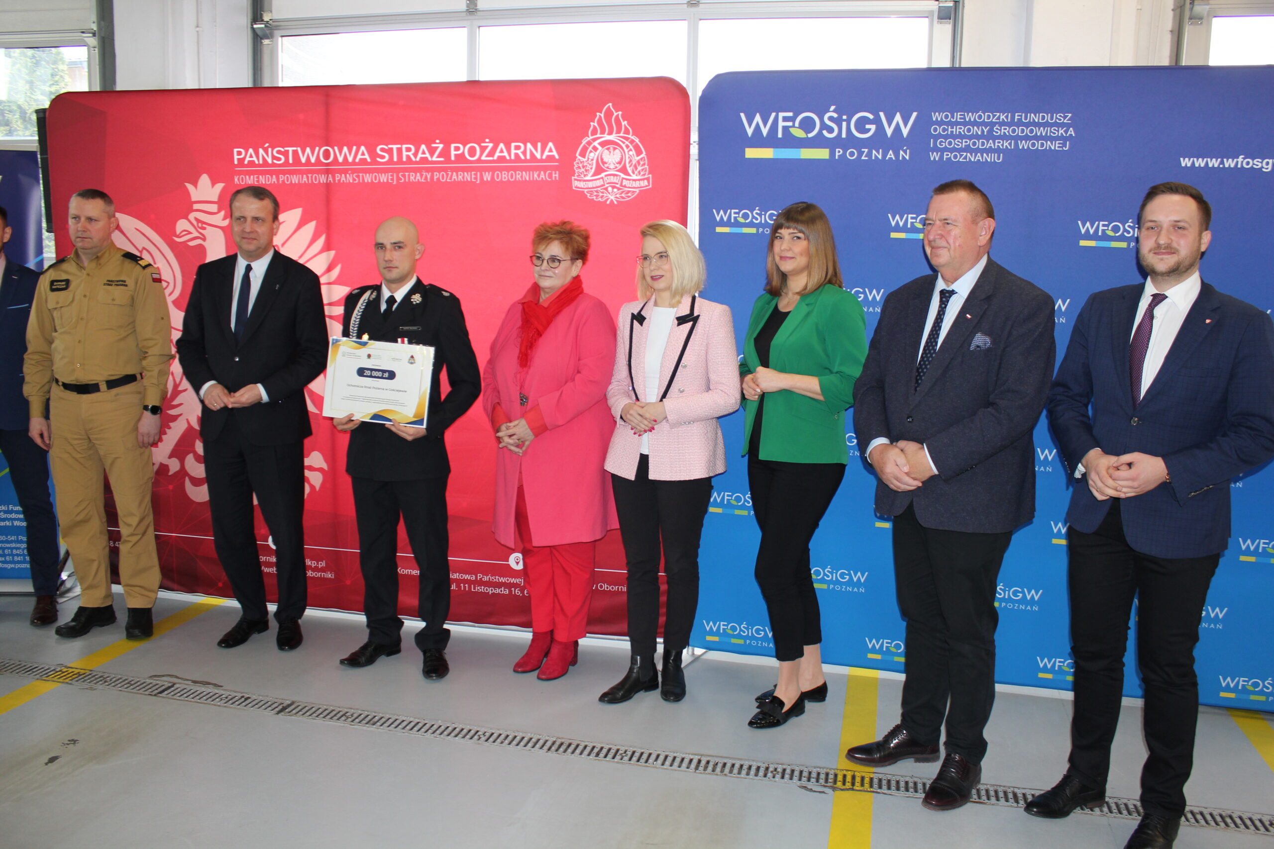 8 osób stoi na tle bannerów reklamowych.