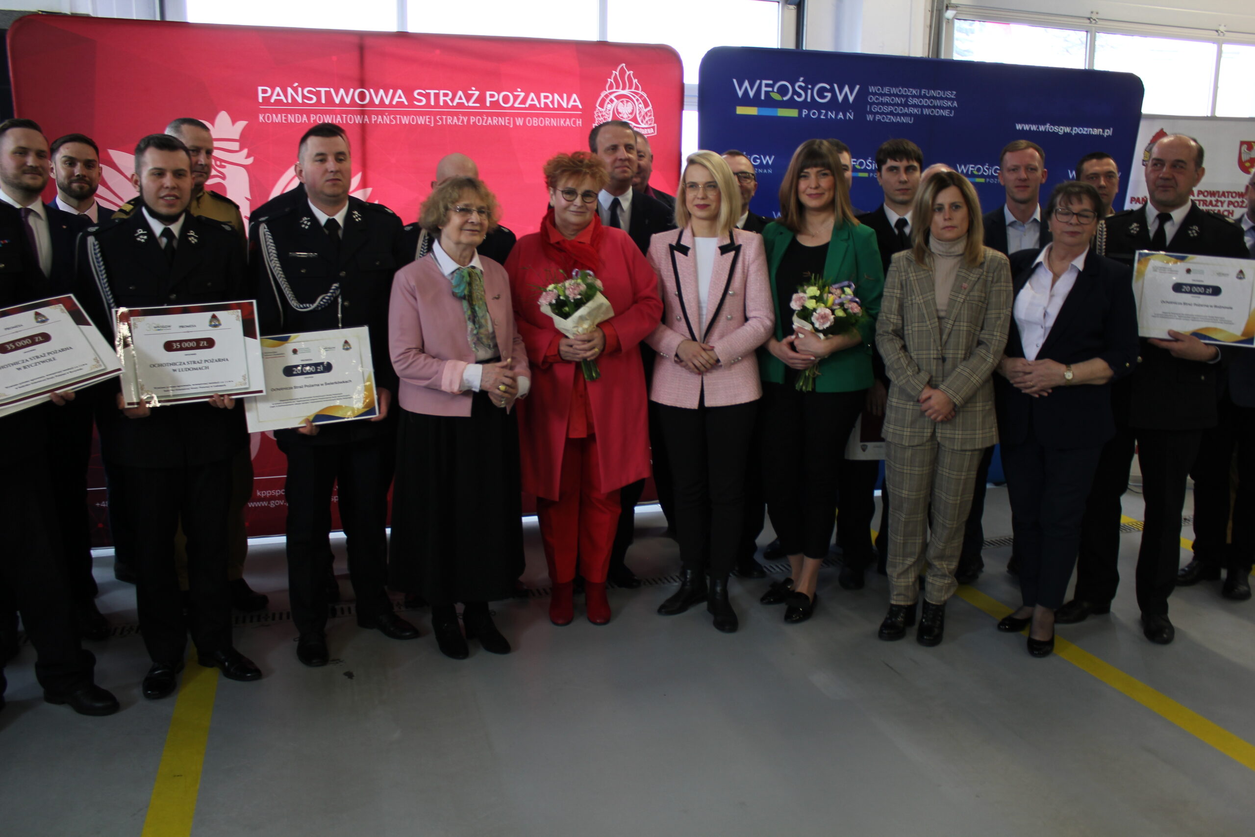 Duża grupa osób stoi na tle bannerów reklamowych.