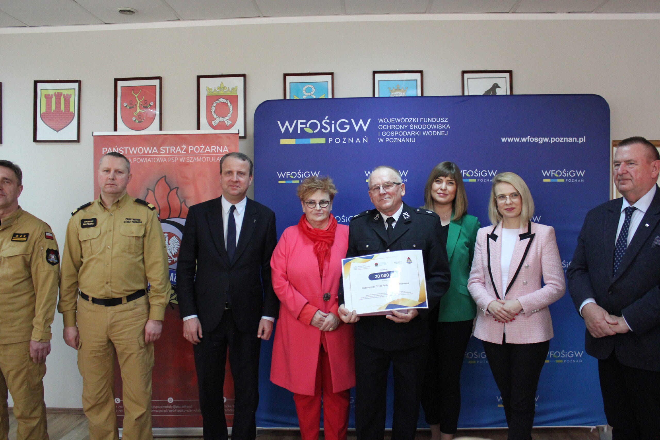 8 osób stoi na tle bannerów reklamowych.