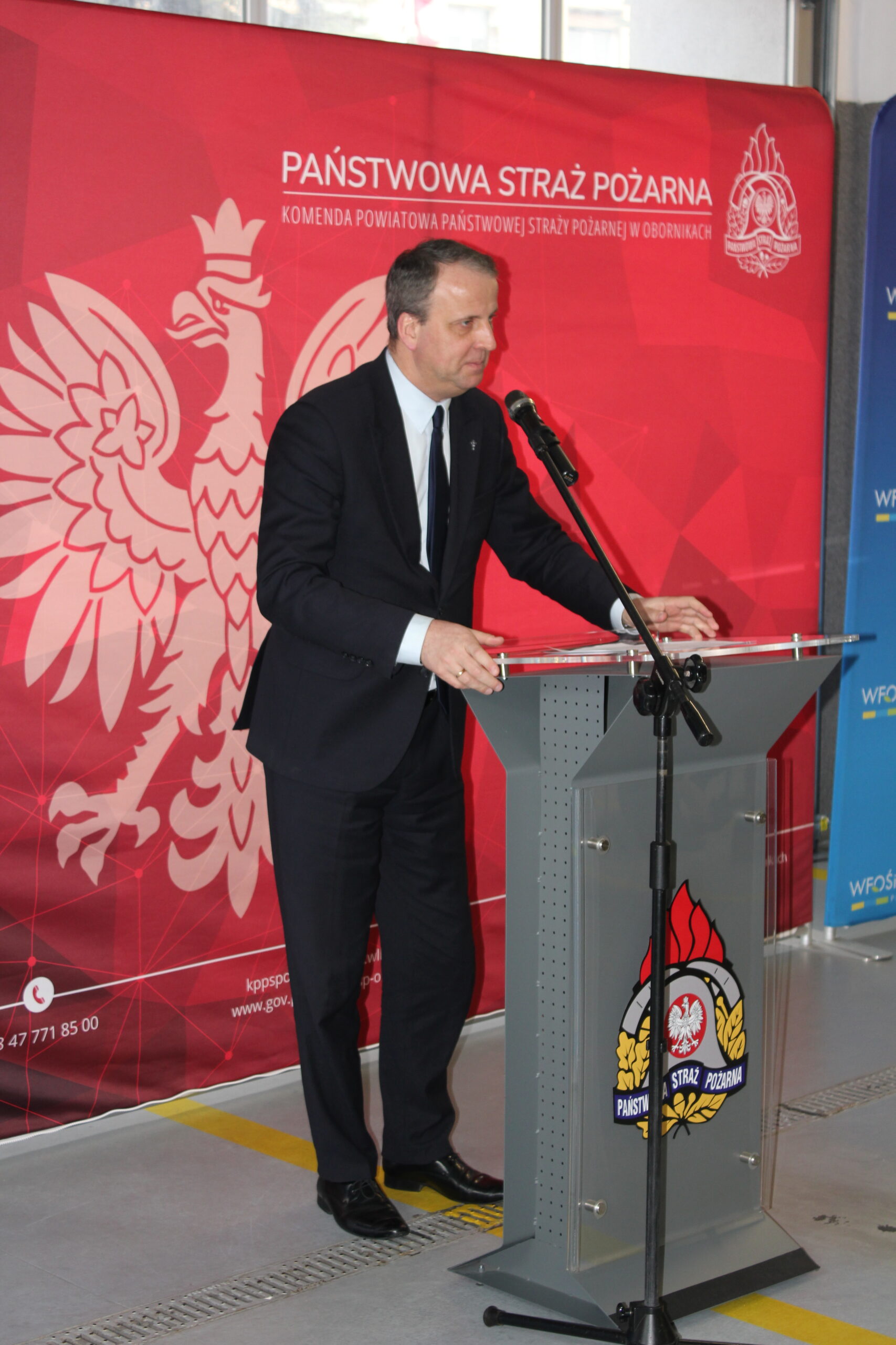 1 osoba stoi przy mównicy i przemawia.