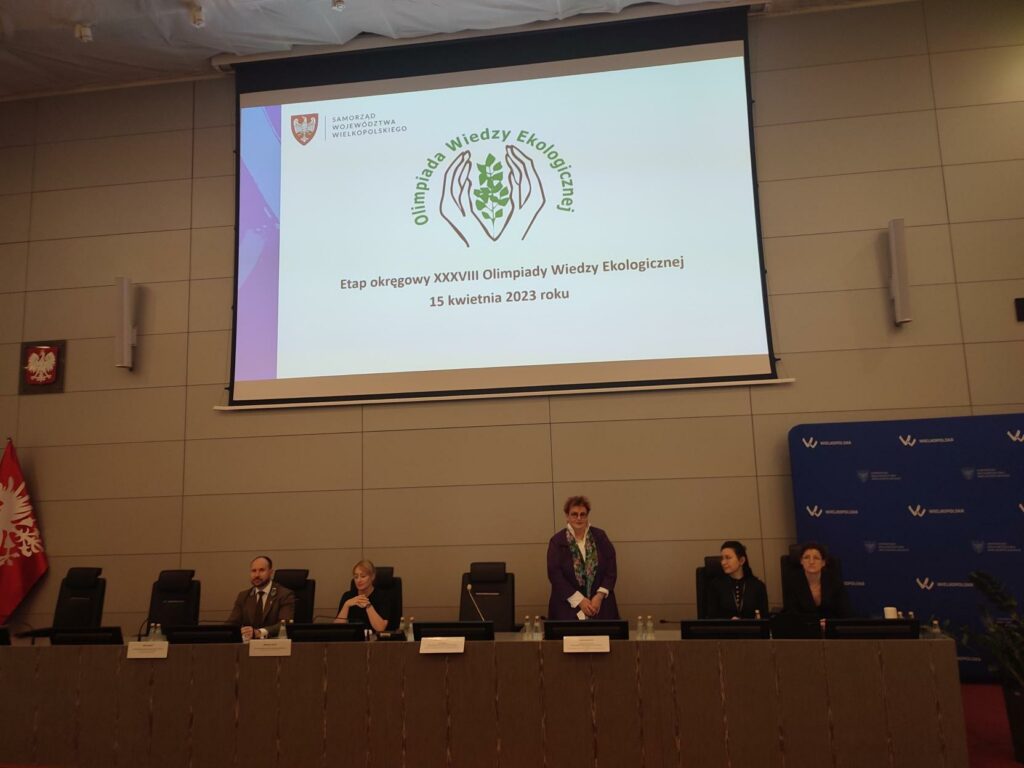 5 osób siedzi przy stole prezydialnym na wielkiej sali.