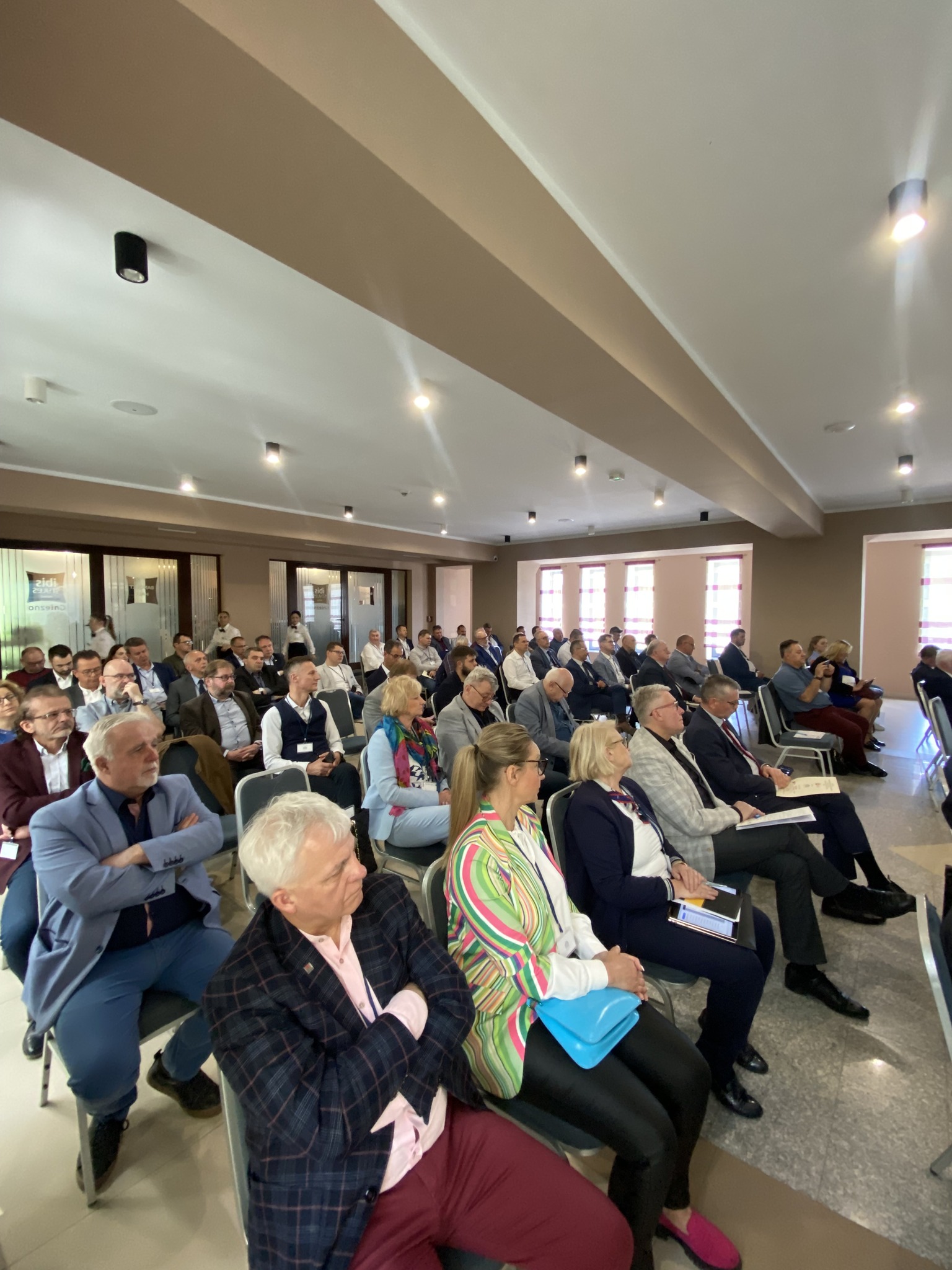 Sala konferencyjna wypełniona ludźmi siedzącymi na krzesłach.