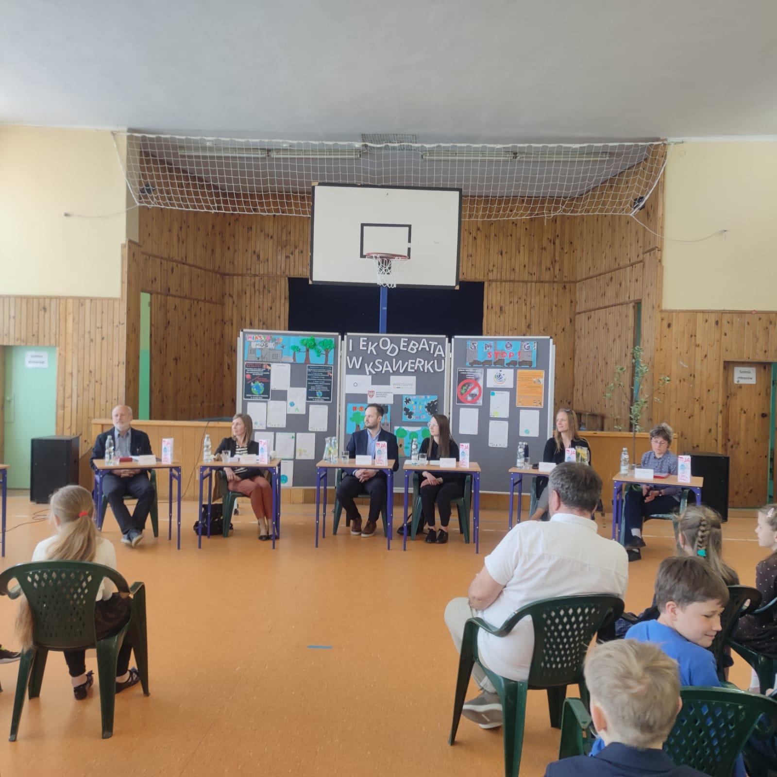 Sala wypełniona dziećmi, a na środku przy stole siedzą dorośli.