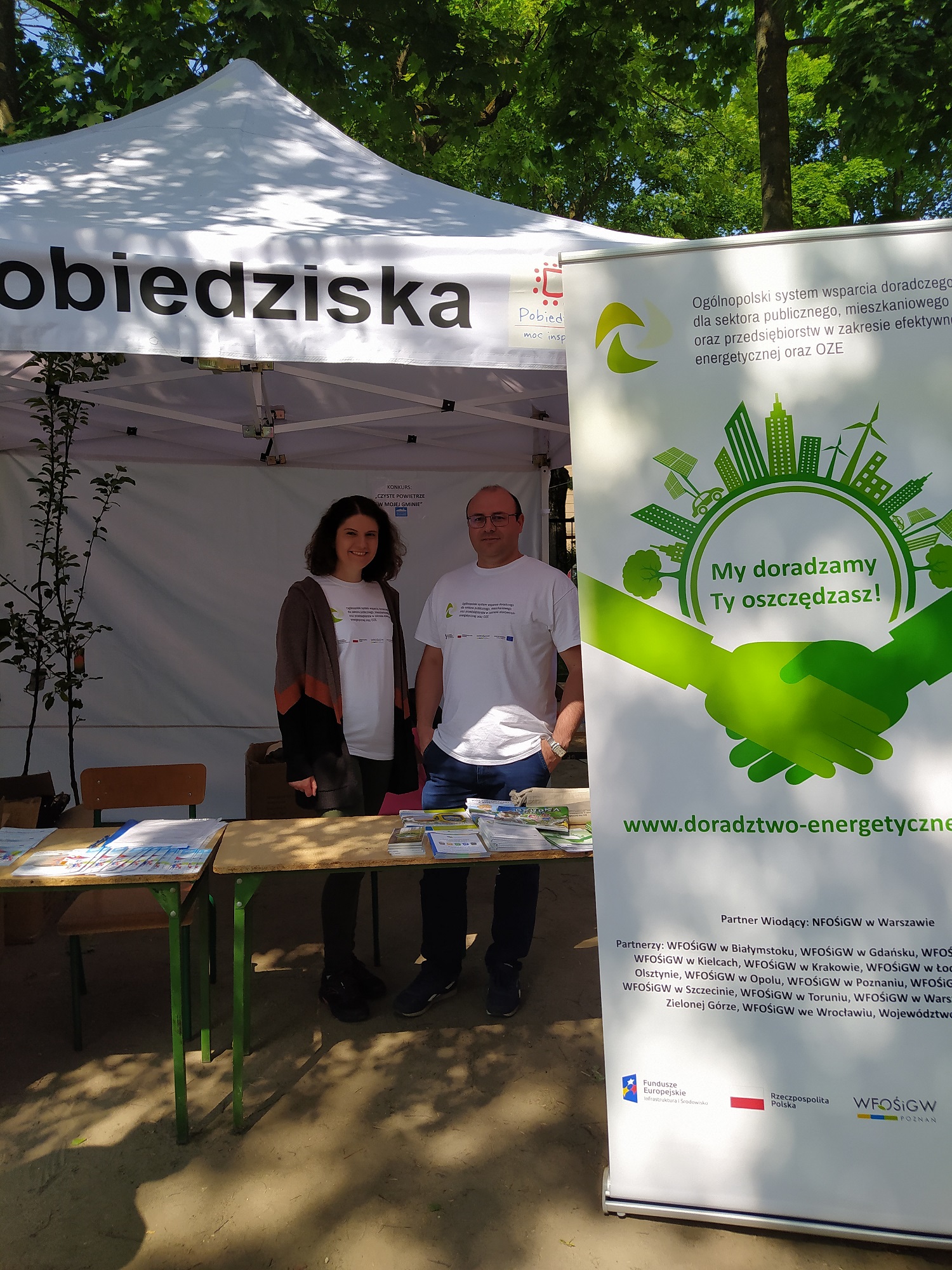 Namiot wystawienniczy i stoisko wystawiennicze i 2 osoby na nim.