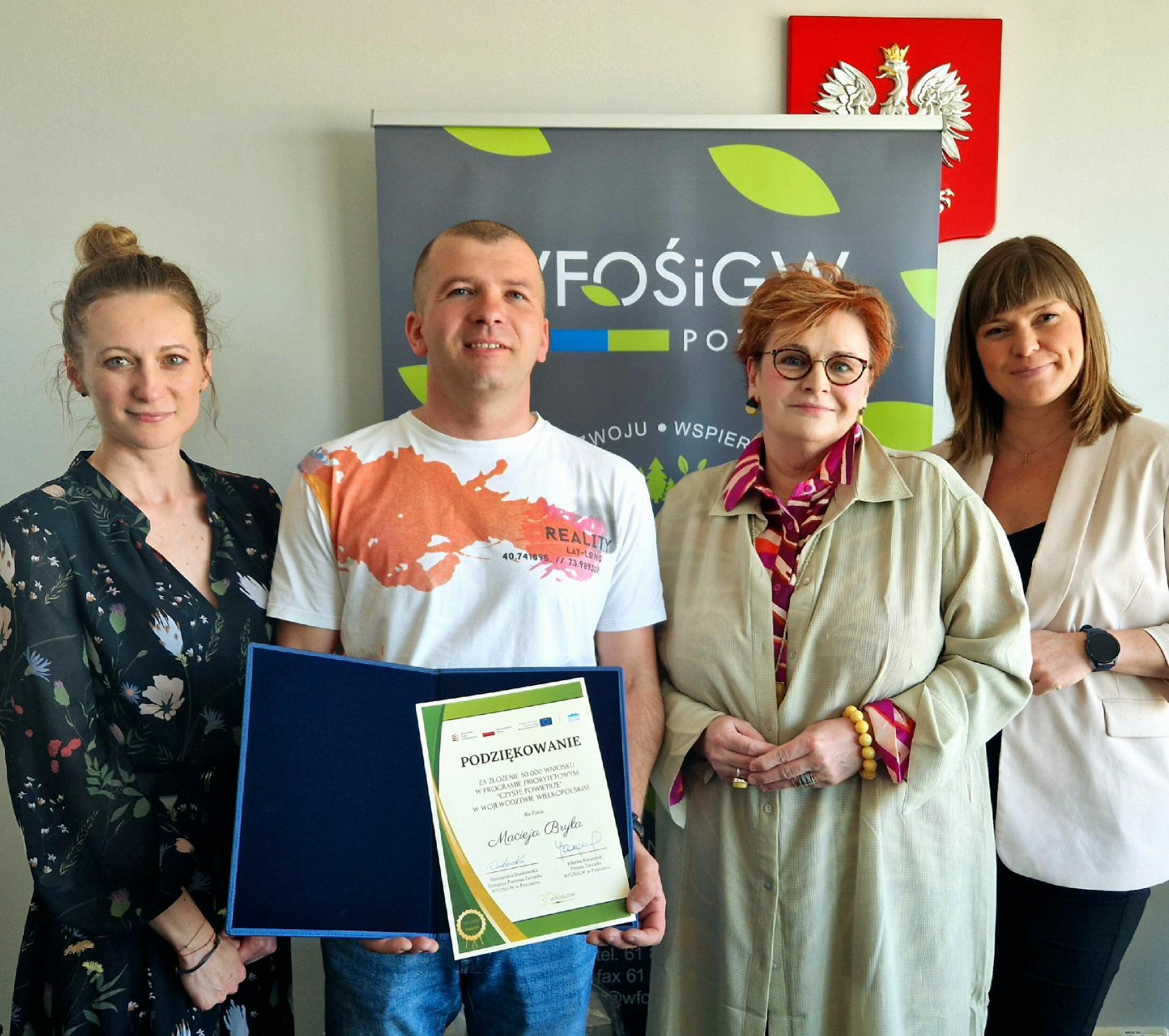 4 osoby stoją na tle ściany i bannera reklamowego.