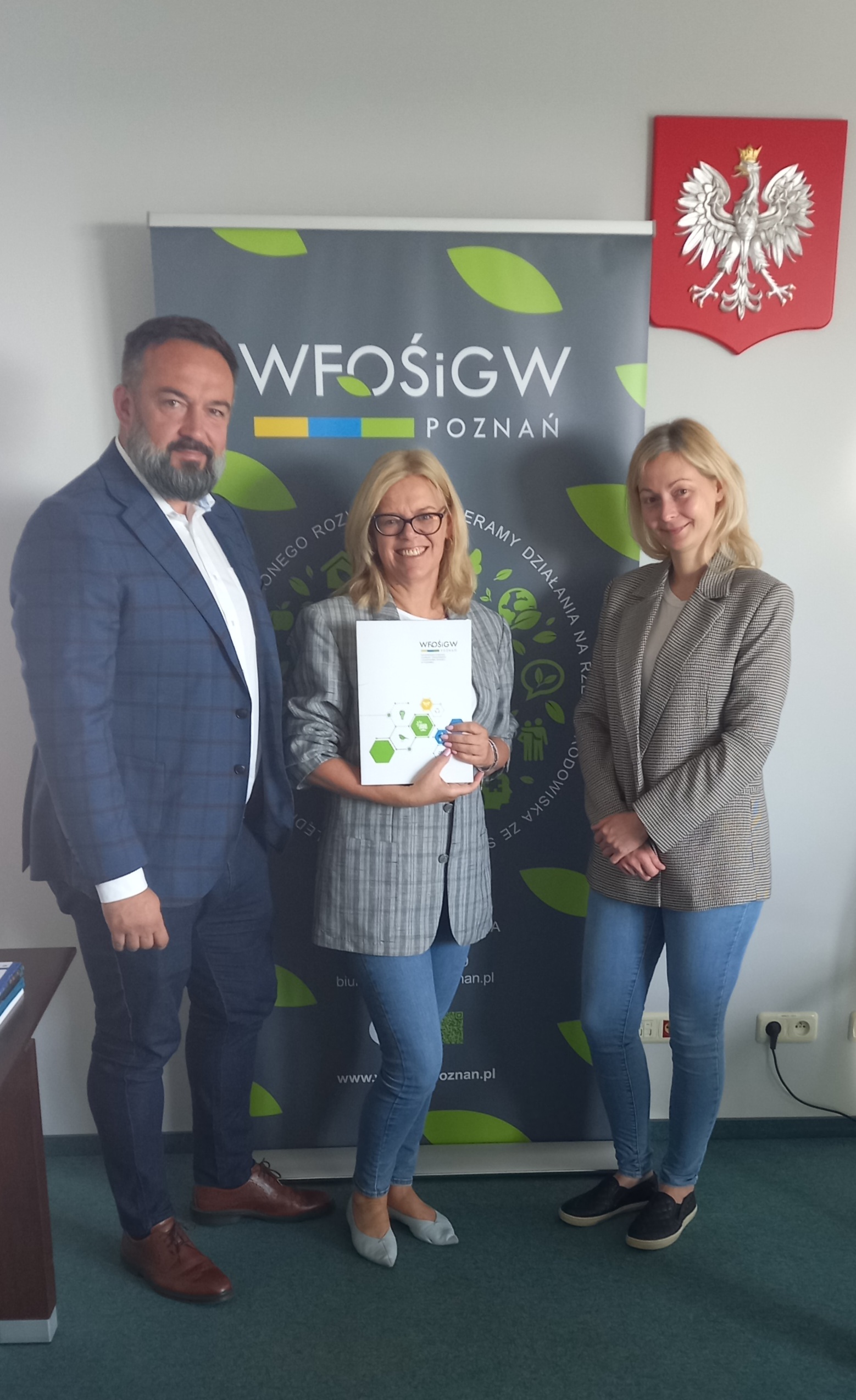 3 osoby stoją na tle bannera reklamowego