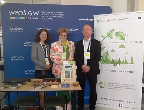 3 osoby stoją na tle ścianki reklamowej