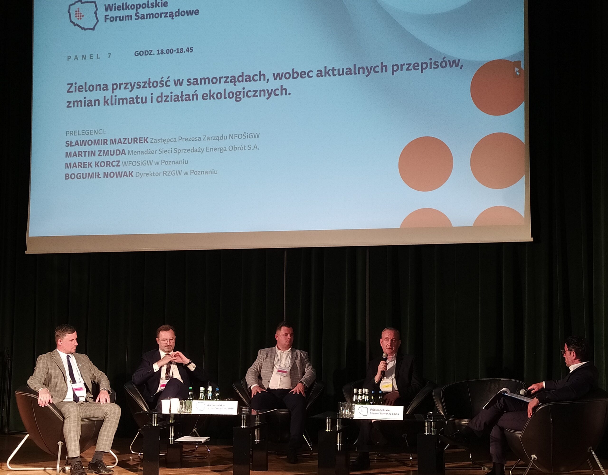 4 osoby siedzą na tle telebimu