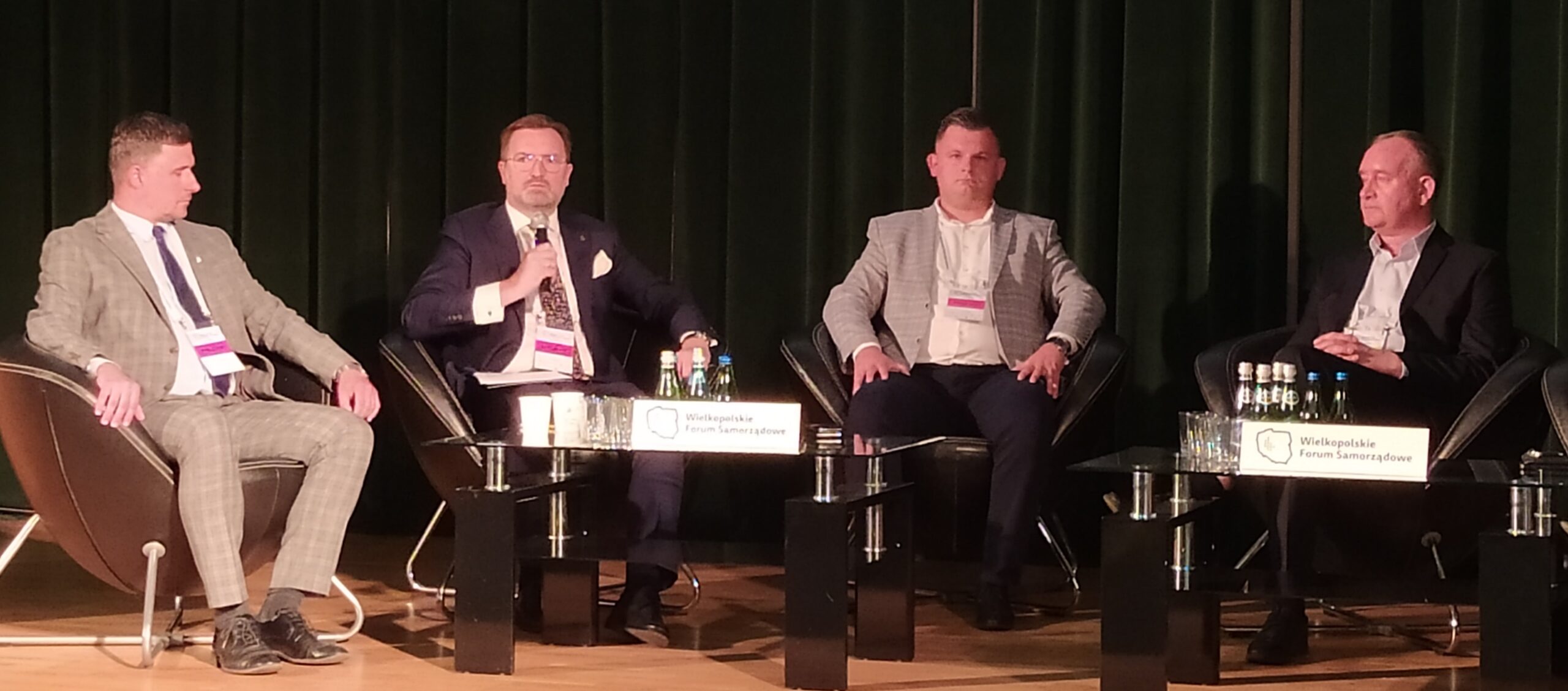 4 osoby siedzą na tle telebimu