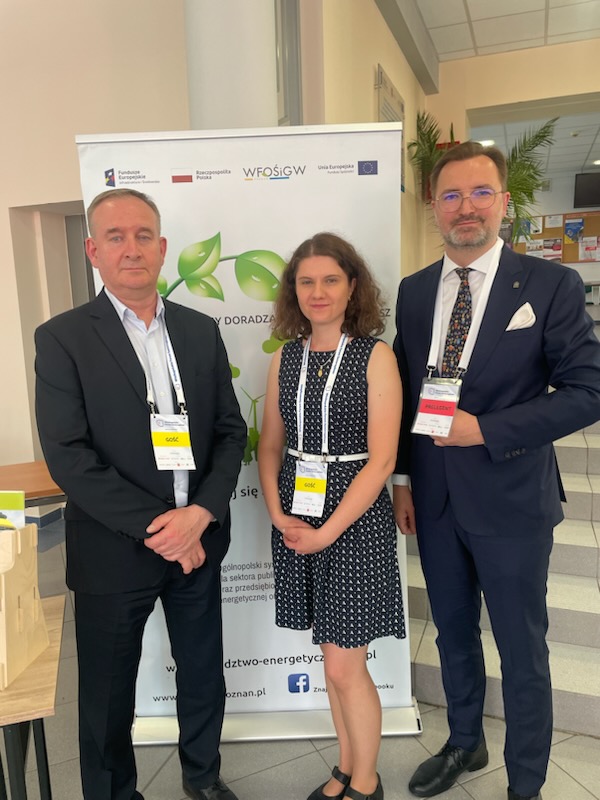 3 osoby stoją na tle bannera reklamowego