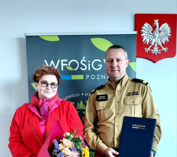 2 osoby stoją na tle bannera reklamowego.