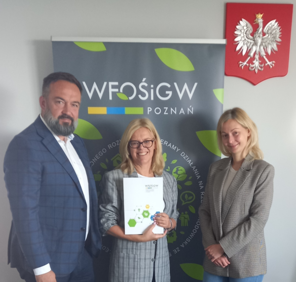 3 osoby stoją na tle bannera reklamowego