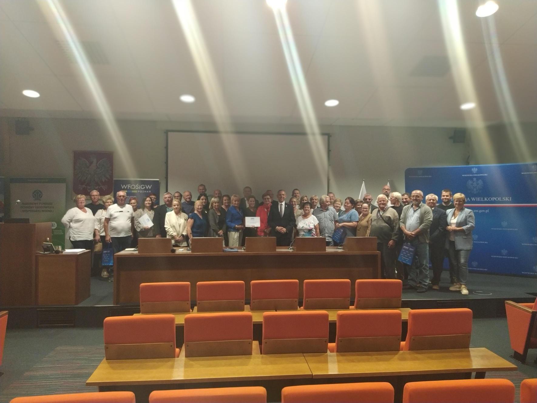 Grupa osób stoi na tle ściany.