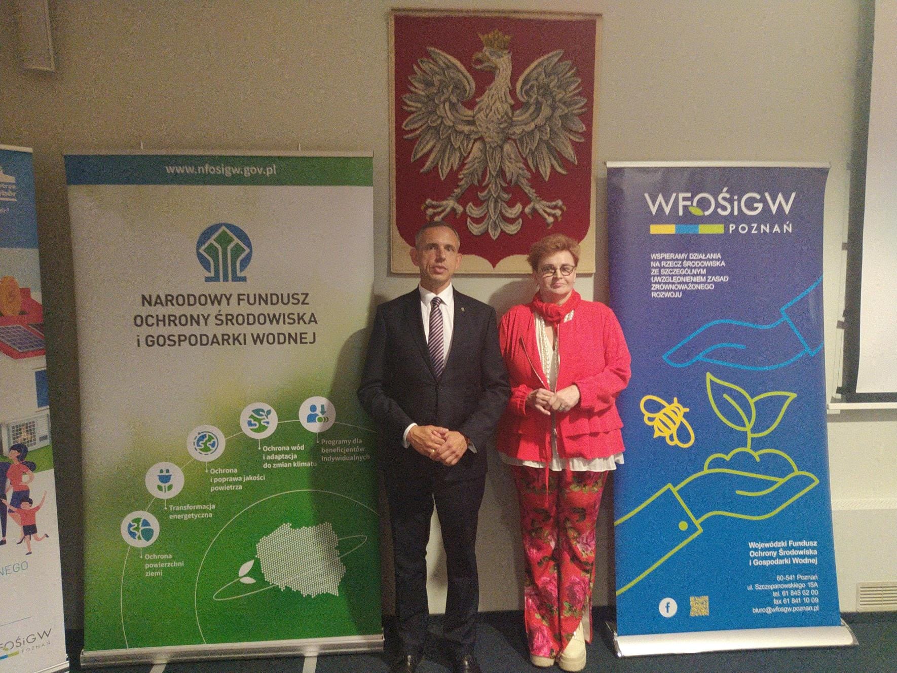 2 osoby stoją na tle bannerów reklamowych.