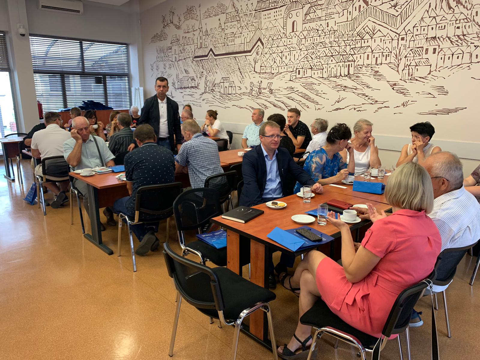 Uczestnicy szkolenia siedzą przy stołach i słuchają.