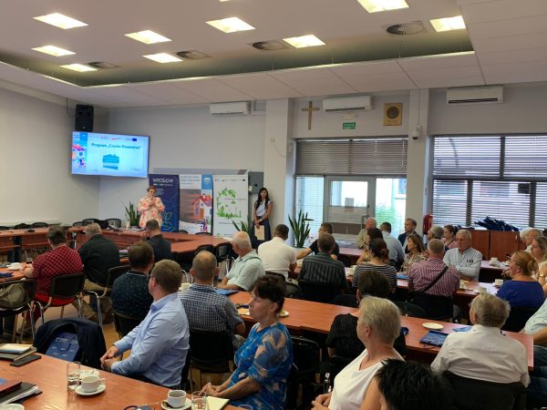 Uczestnicy szkolenia siedzą przy stołach i słuchają.