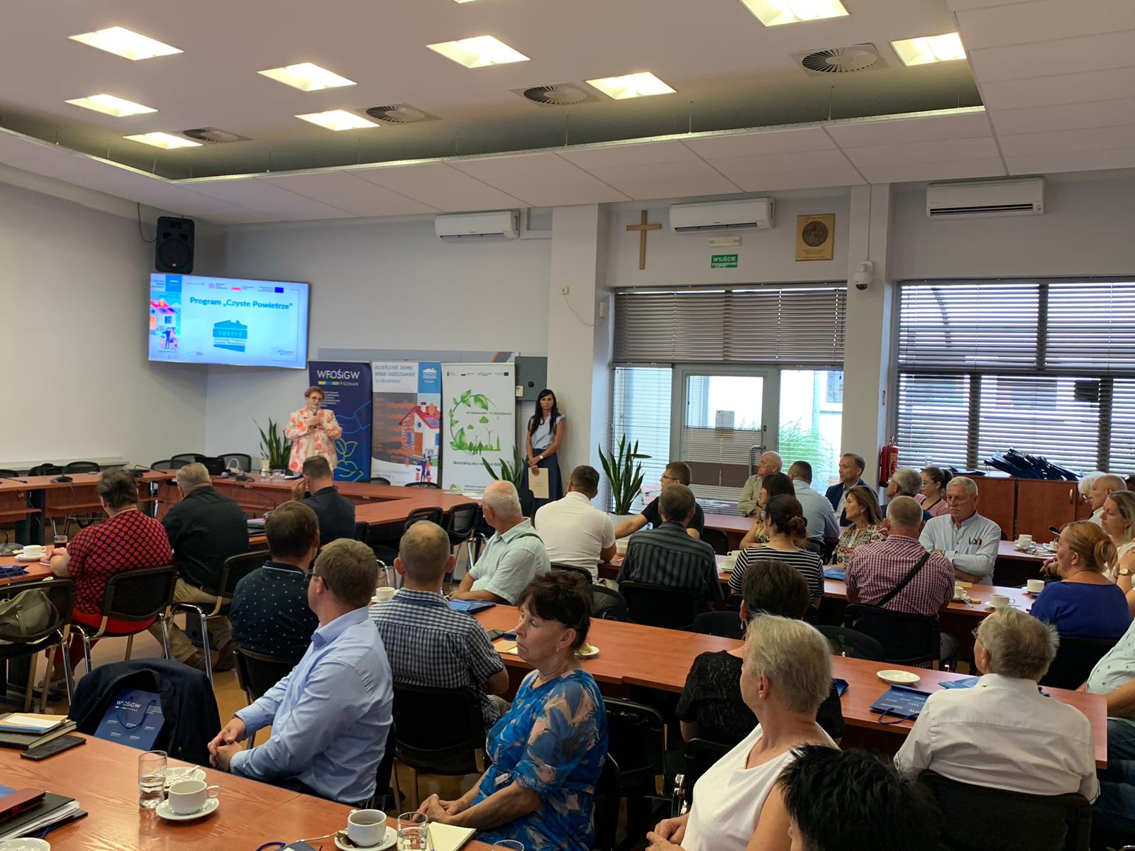 Uczestnicy szkolenia siedzą przy stołach i słuchają.