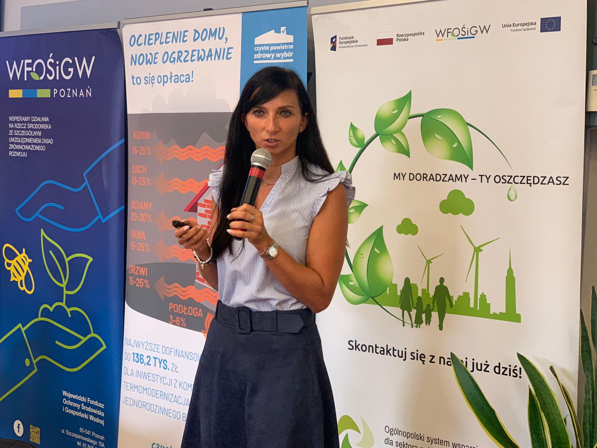 Jedna osoba stoi za stole na tle ściany i przemawia.