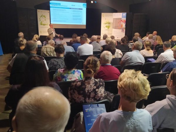 Ludzie siedzą na krzesłach w układzie kinowym, a doradca energetyczny na środku przeprowadza szkolenie.